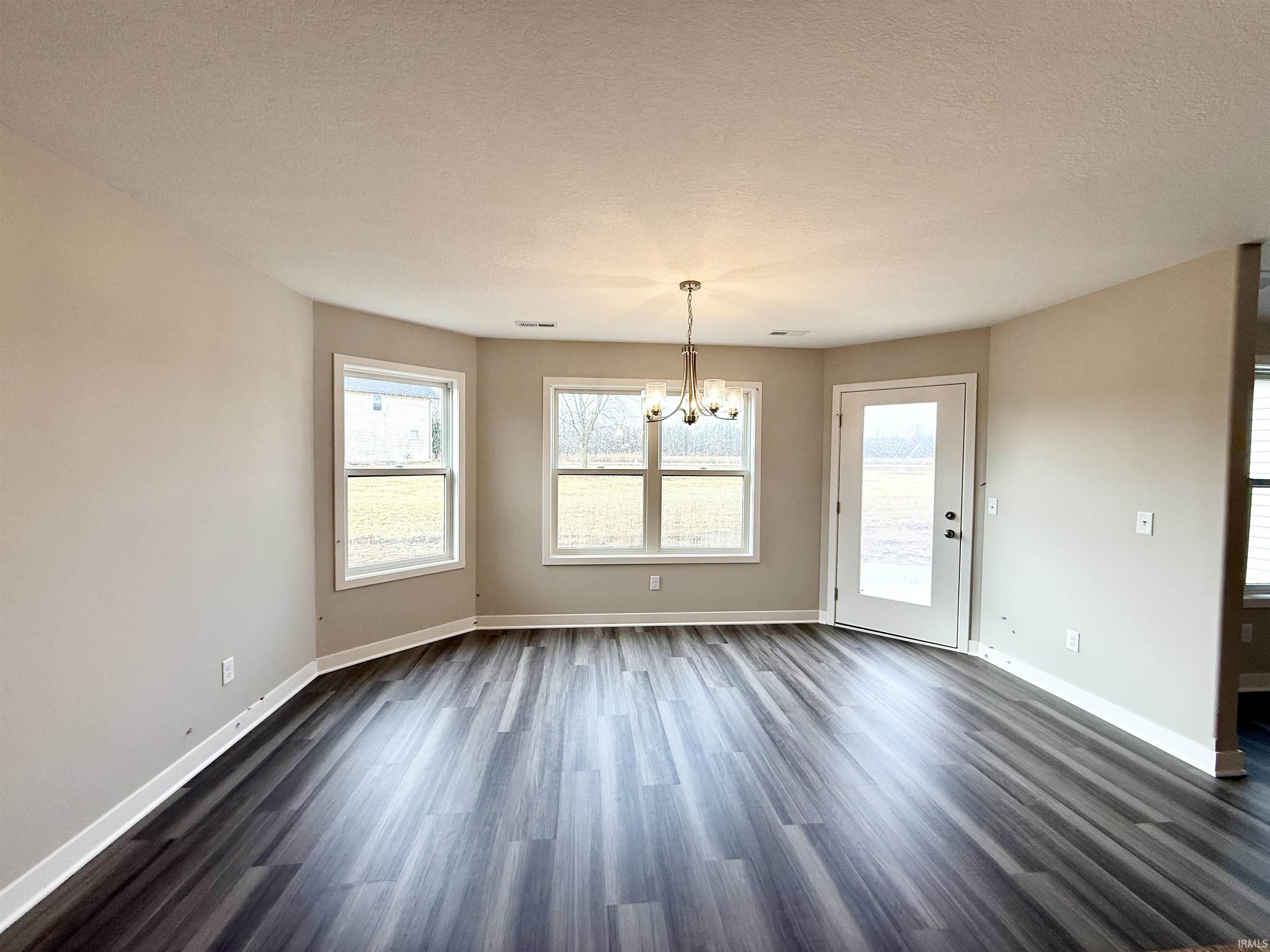 Unfurnished dining area featuring suspended lighting, dark wood-type flooring, and a textured ceiling