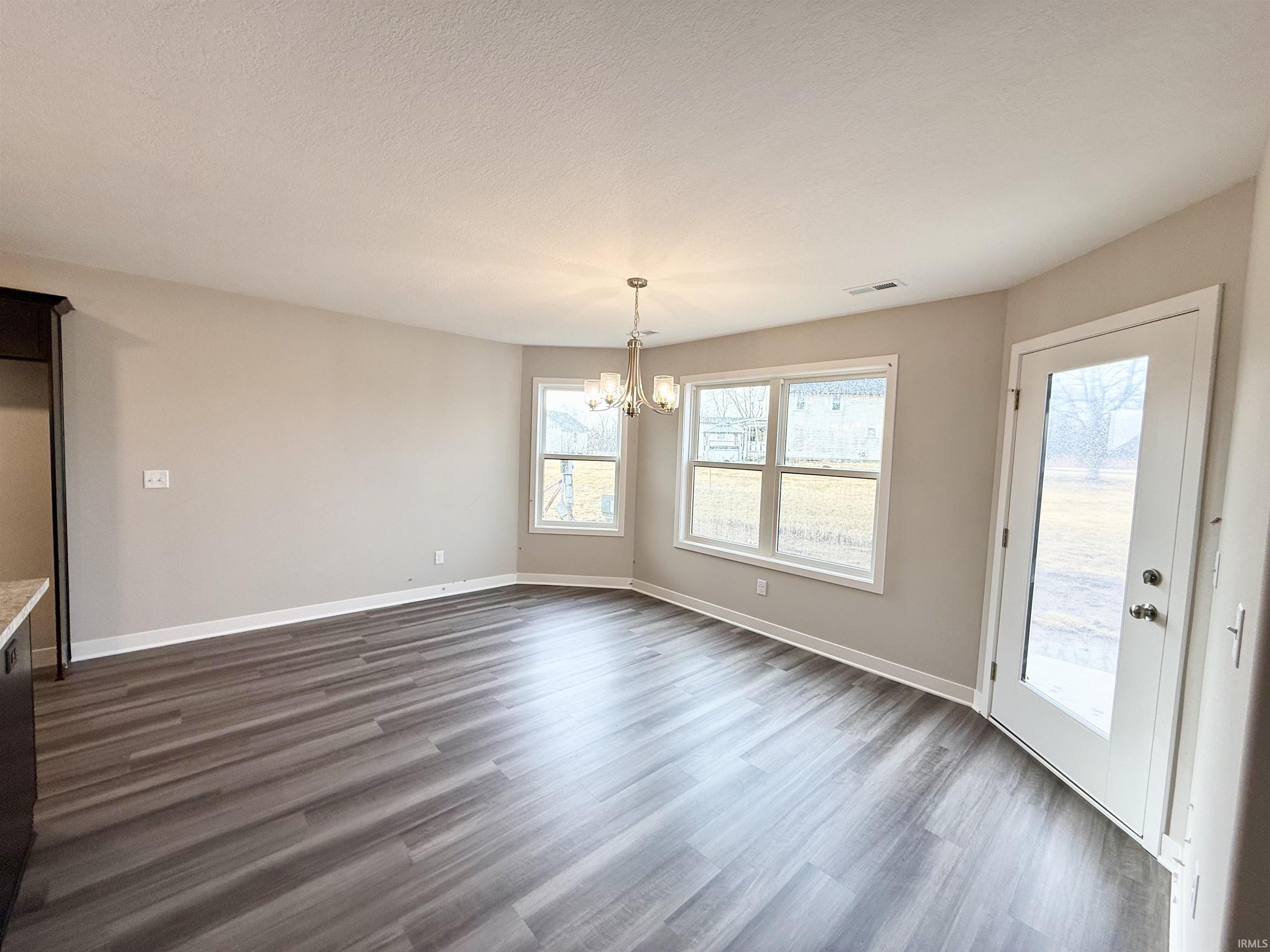 Unfurnished dining area featuring a chandelier, dark wood-type flooring, and a textured ceiling