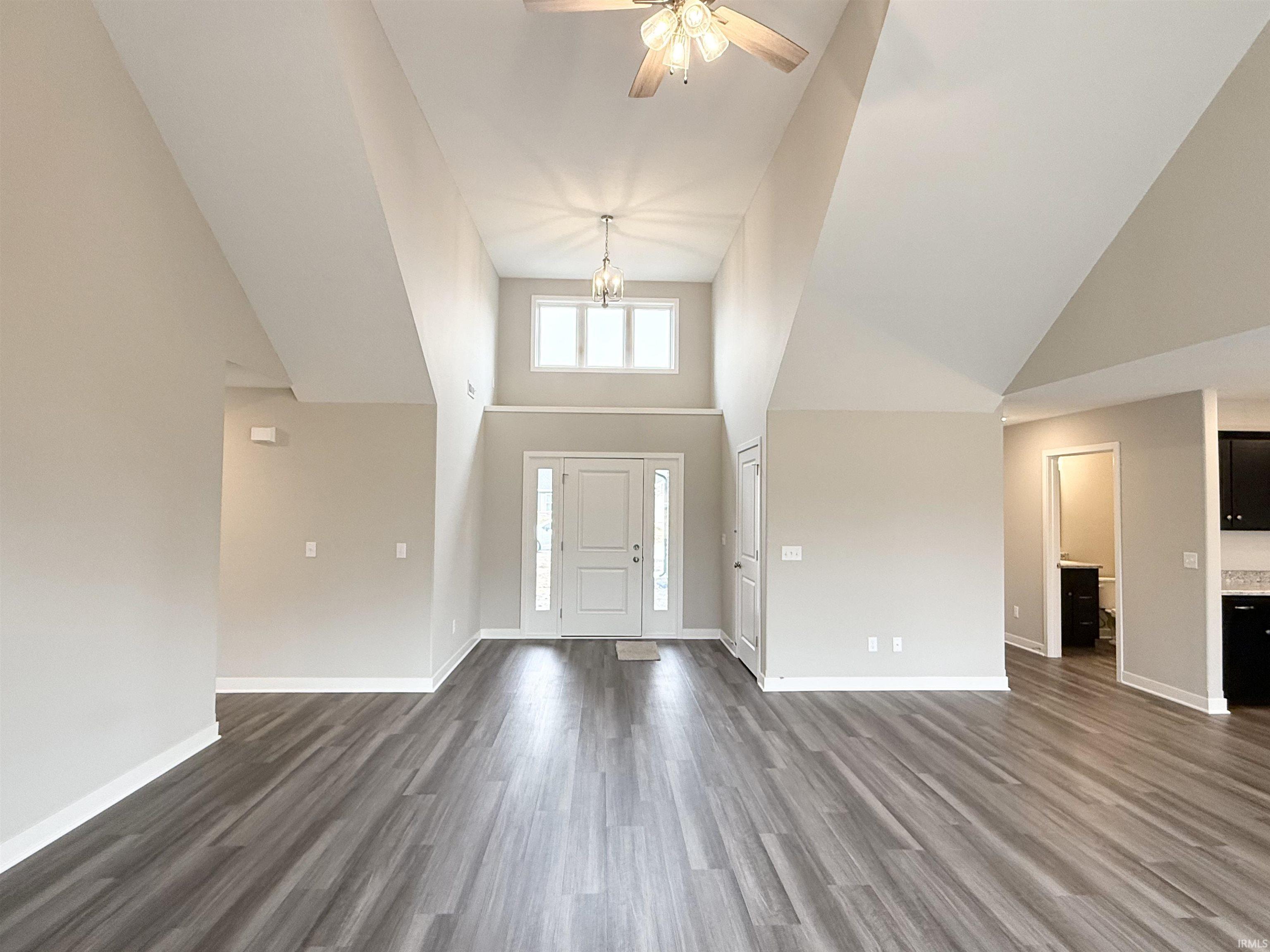 Foyer featuring dark wood-type flooring, a ceiling fan, a chandelier, and lofted ceiling