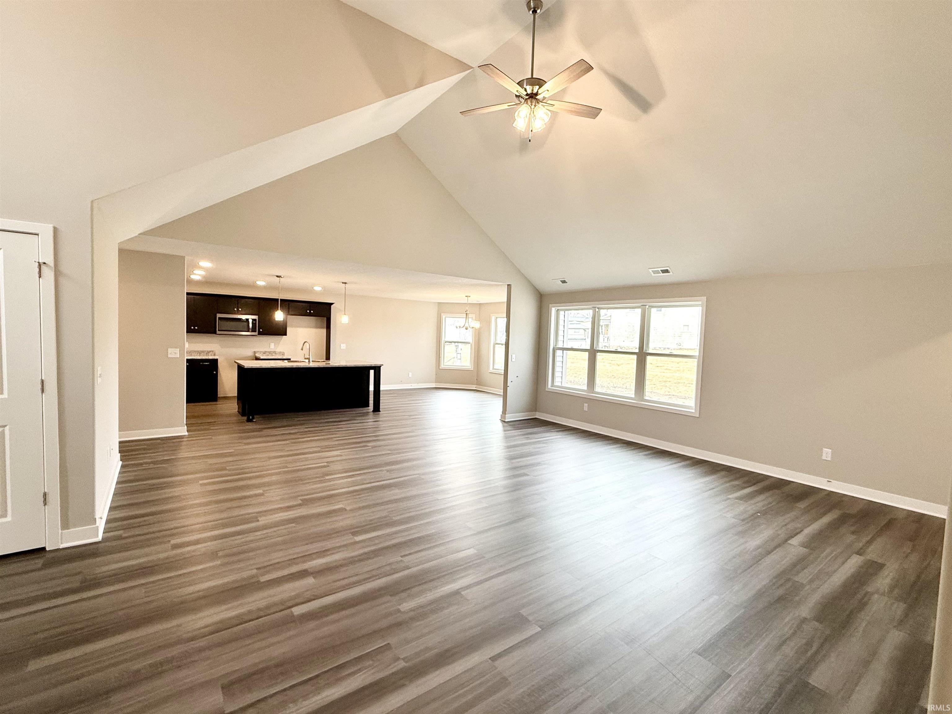 Unfurnished living room with a ceiling fan, dark wood finished floors, lofted ceiling, and suspended lighting