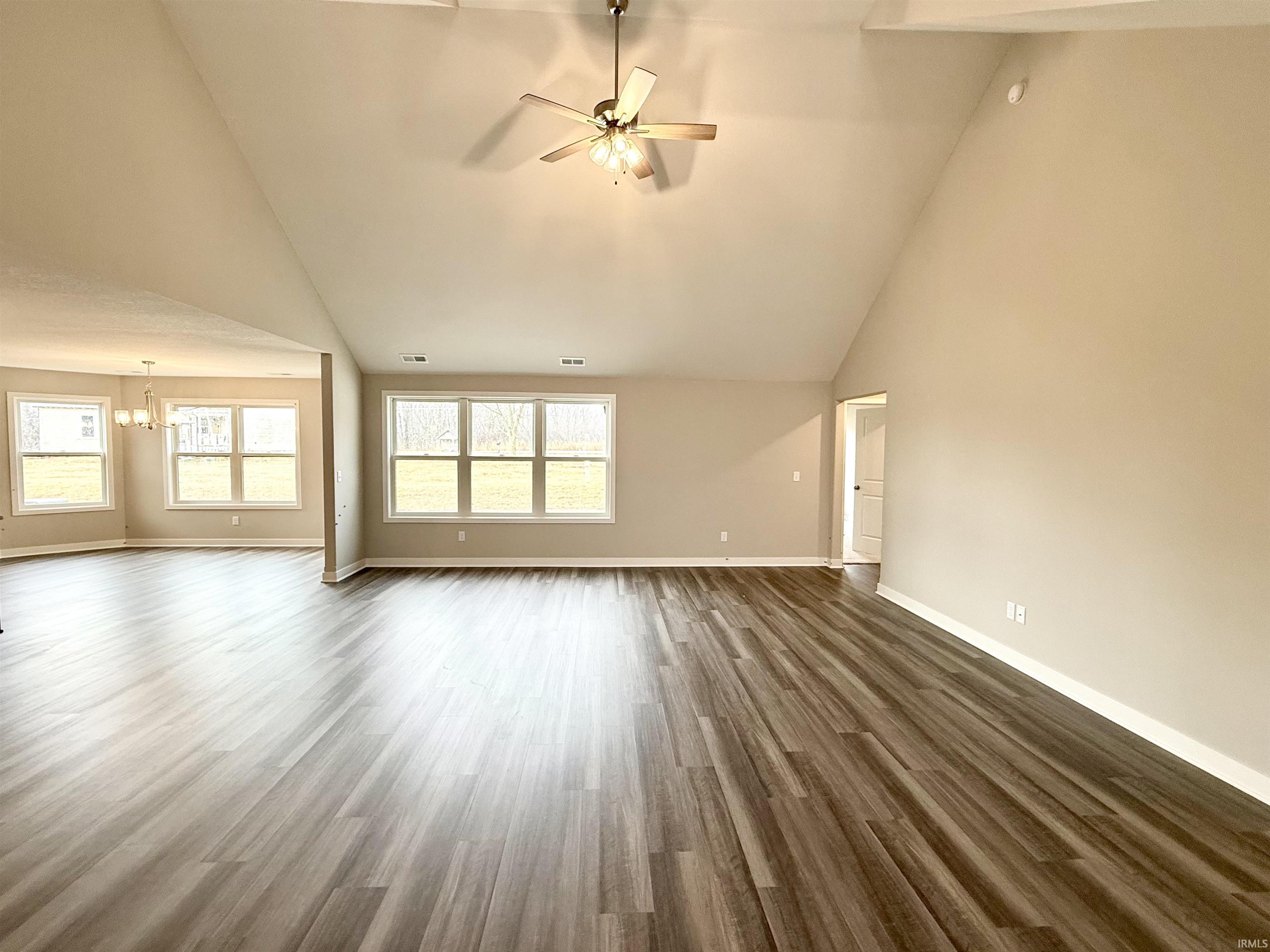 Unfurnished living room with ceiling fan, dark wood-style floors, lofted ceiling, and hanging lights