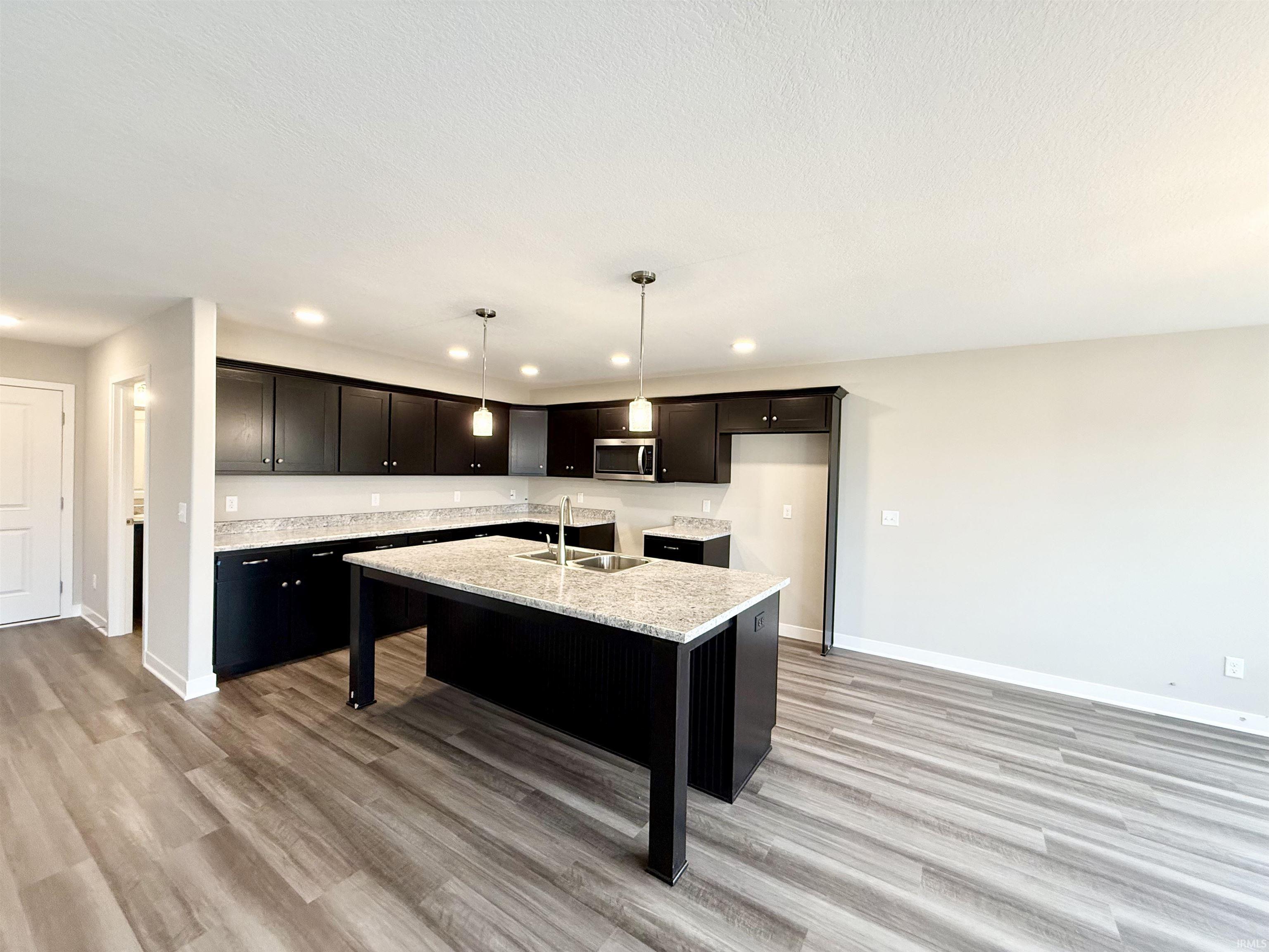 Kitchen featuring a kitchen breakfast bar, light stone countertops, a center island with sink, light wood-style floors, and stainless steel microwave