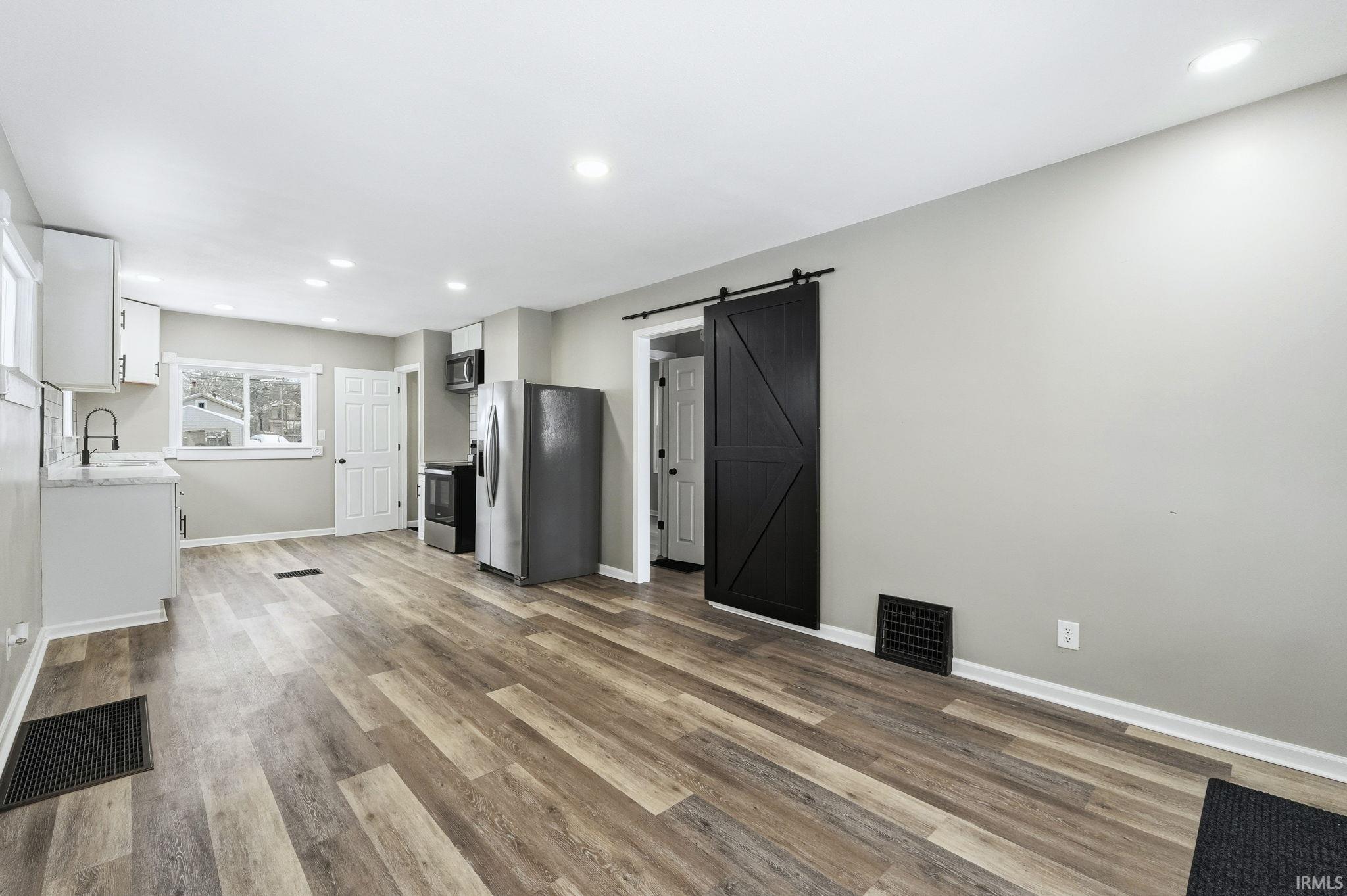 Unfurnished living room featuring a barn door, recessed lighting, and light wood finished floors