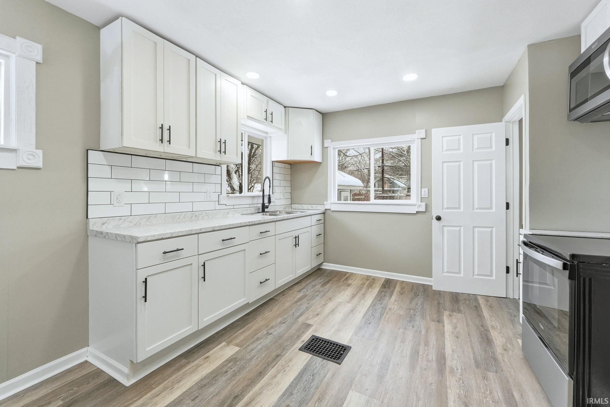 Kitchen featuring appliances with stainless steel finishes, white cabinetry, decorative backsplash, light wood finished floors, and recessed lighting