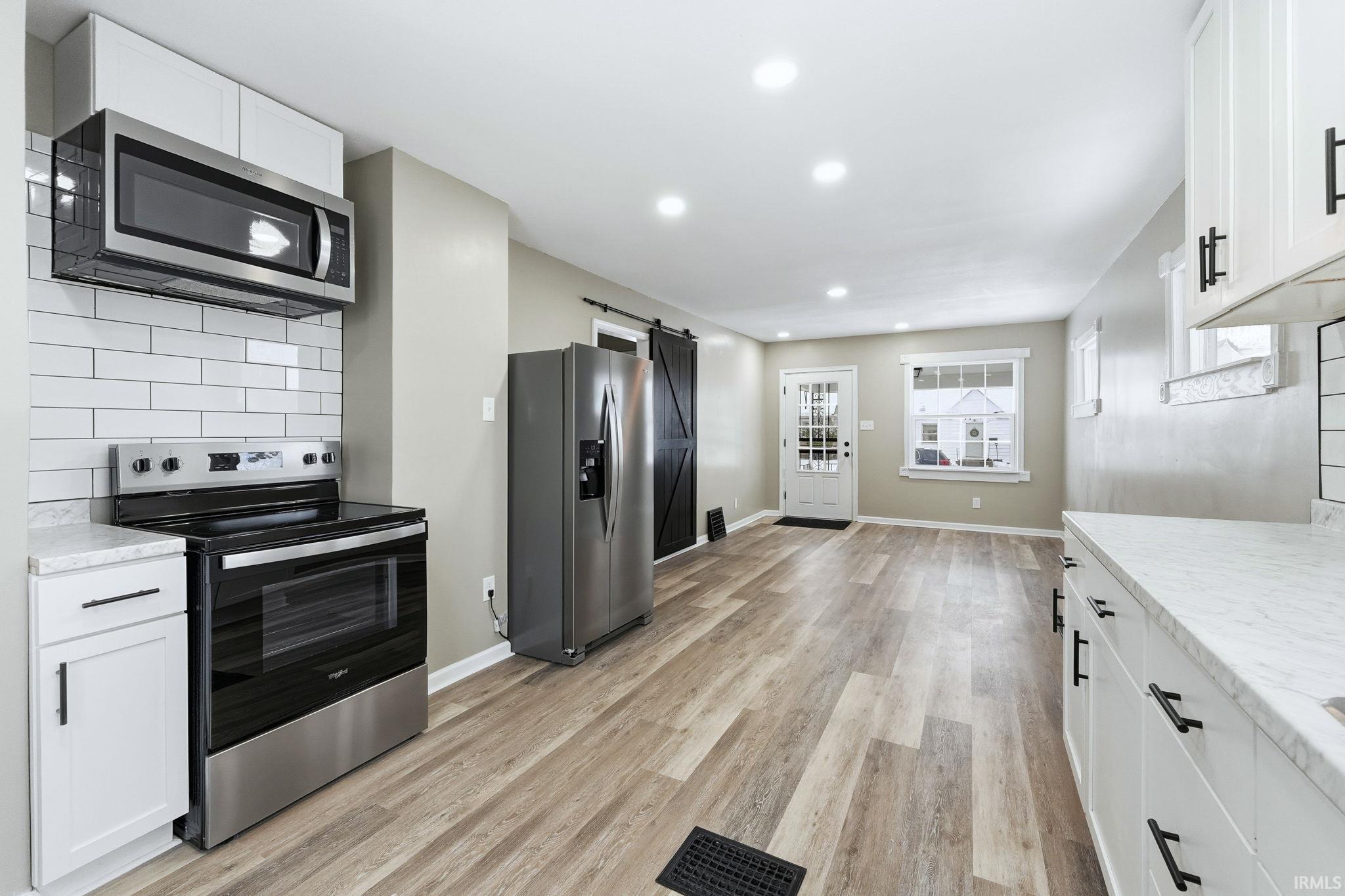 Kitchen with a barn door, decorative backsplash, stainless steel appliances, white cabinets, and recessed lighting