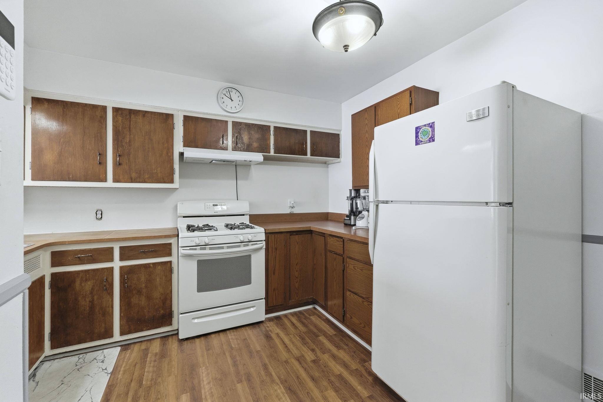 Kitchen with white appliances, open shelves, dark wood finished floors, under cabinet range hood, and light countertops
