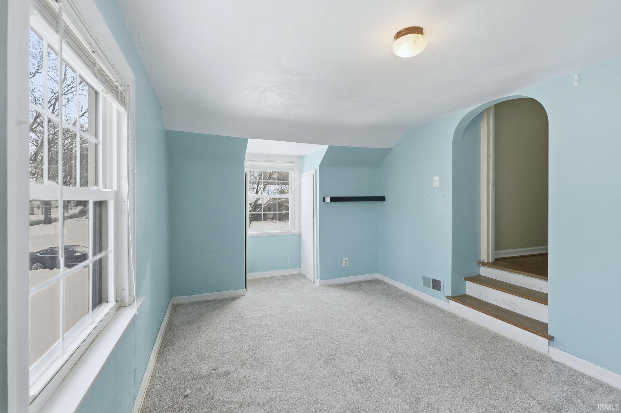 Spare room featuring light colored carpet, arched walkways, and lofted ceiling