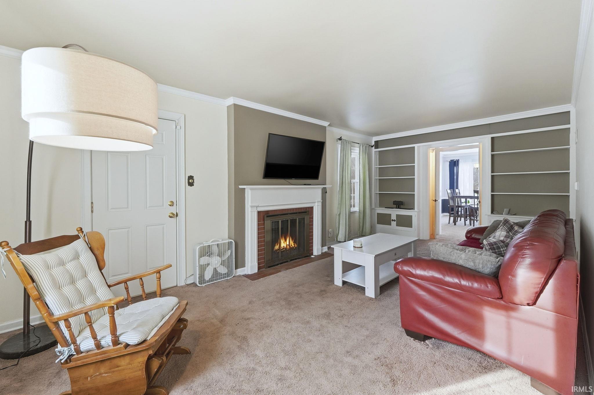 Carpeted living area featuring crown molding, a fireplace, and built in features