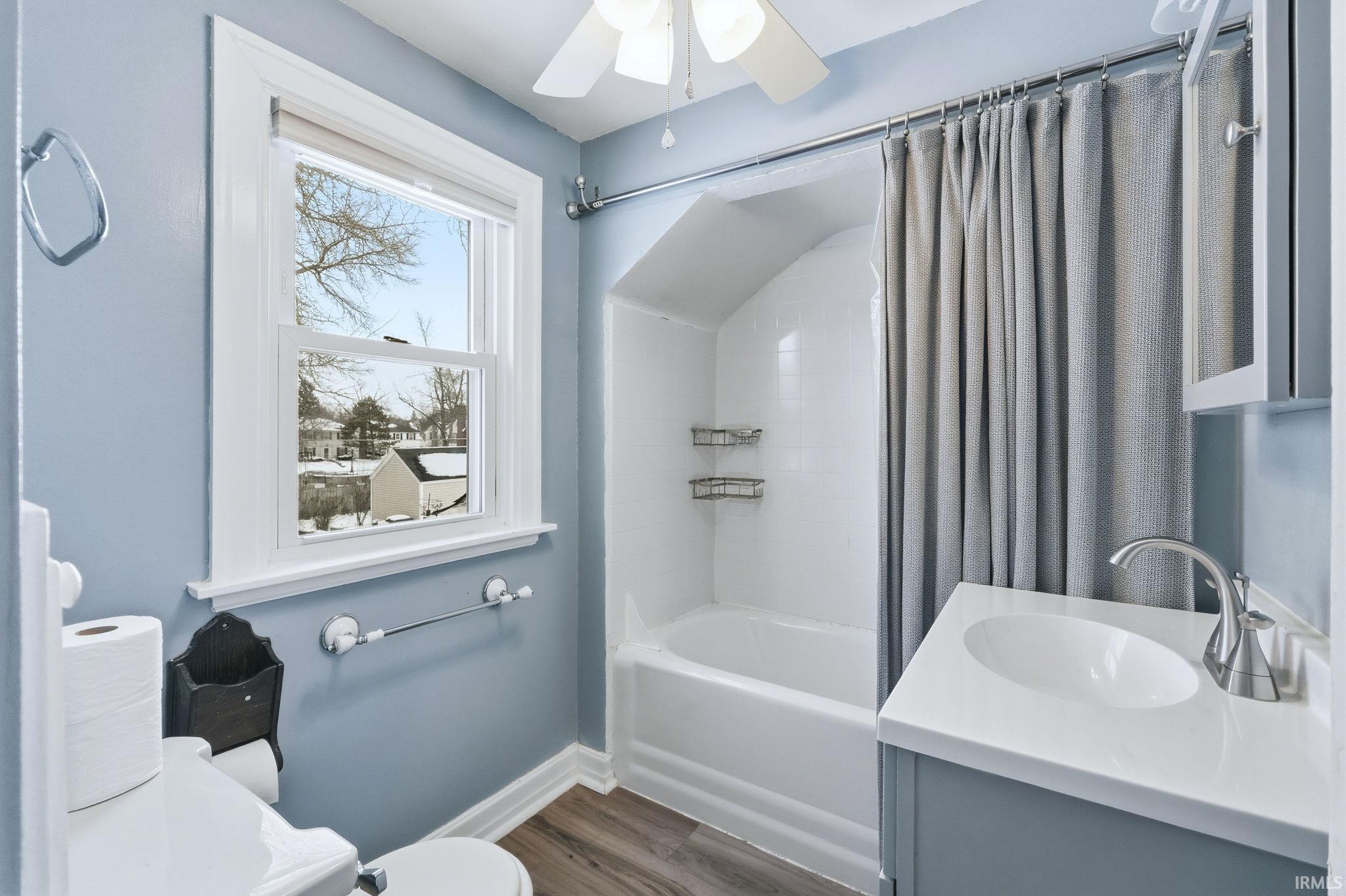 Full bathroom featuring vanity, shower / bath combo with shower curtain, dark wood-type flooring, and ceiling fan