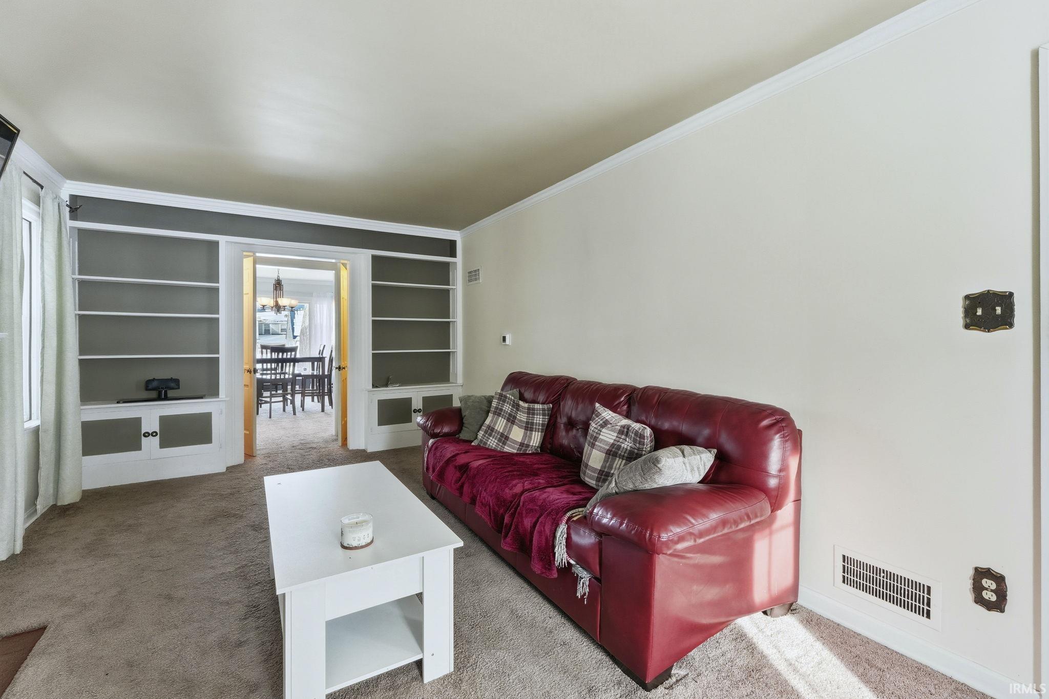 Living area with carpet flooring, built in features, and crown molding