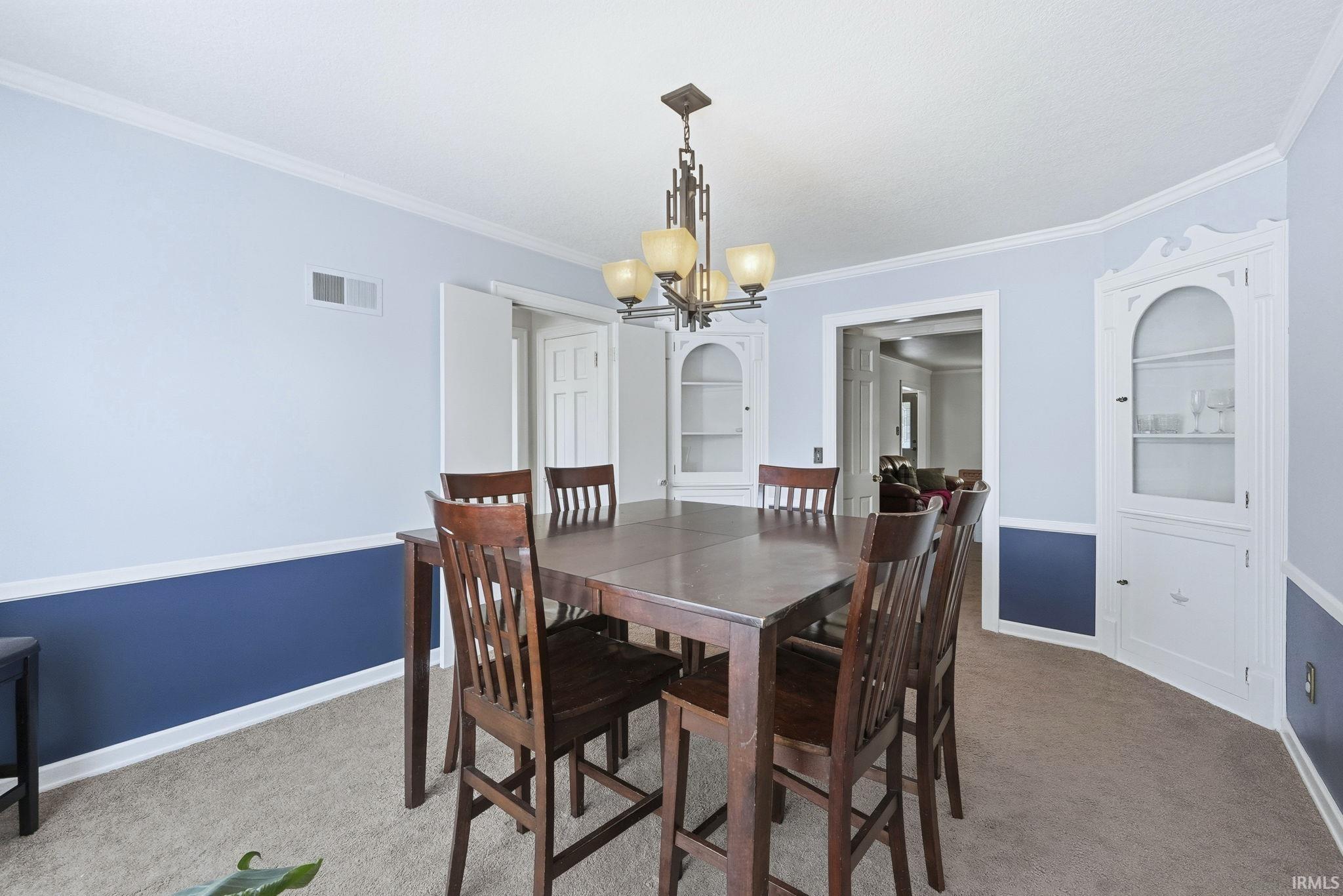 Dining room featuring ornamental molding, a chandelier, and light colored carpet