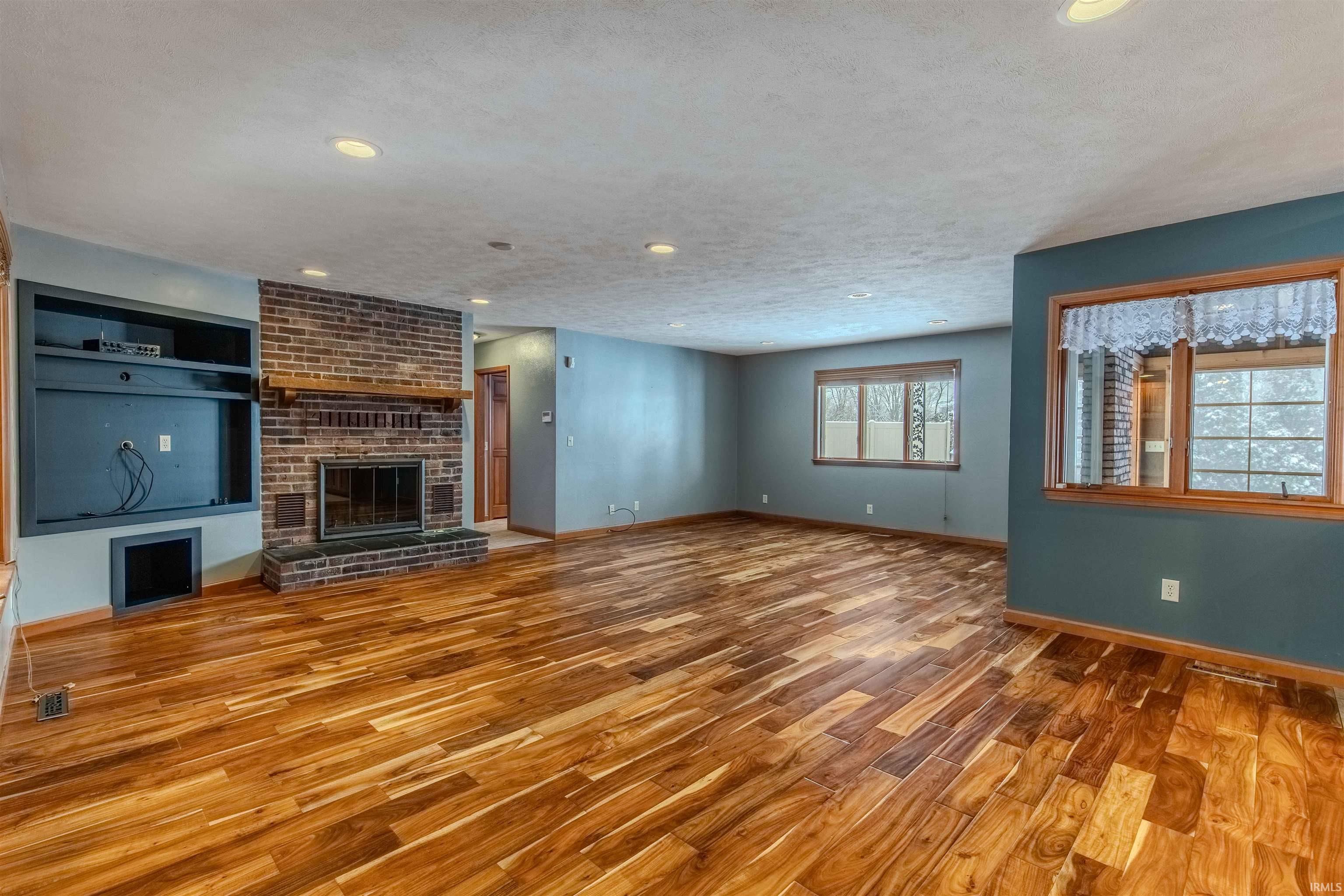 Unfurnished living room with wood finished floors, a brick fireplace, a textured ceiling, and recessed lighting