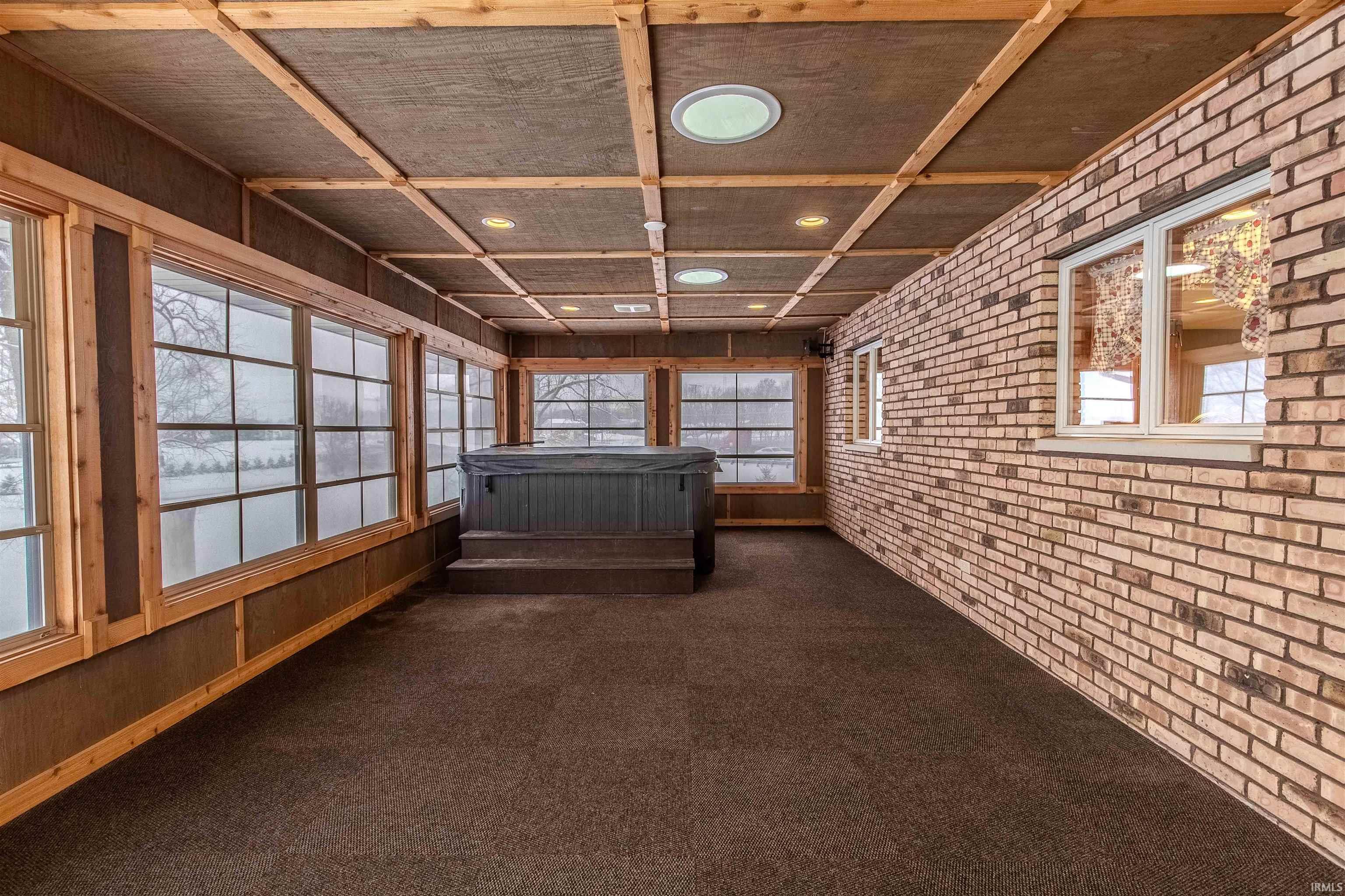 Unfurnished sunroom with a jacuzzi, plenty of natural light, brick wall, and carpet floors