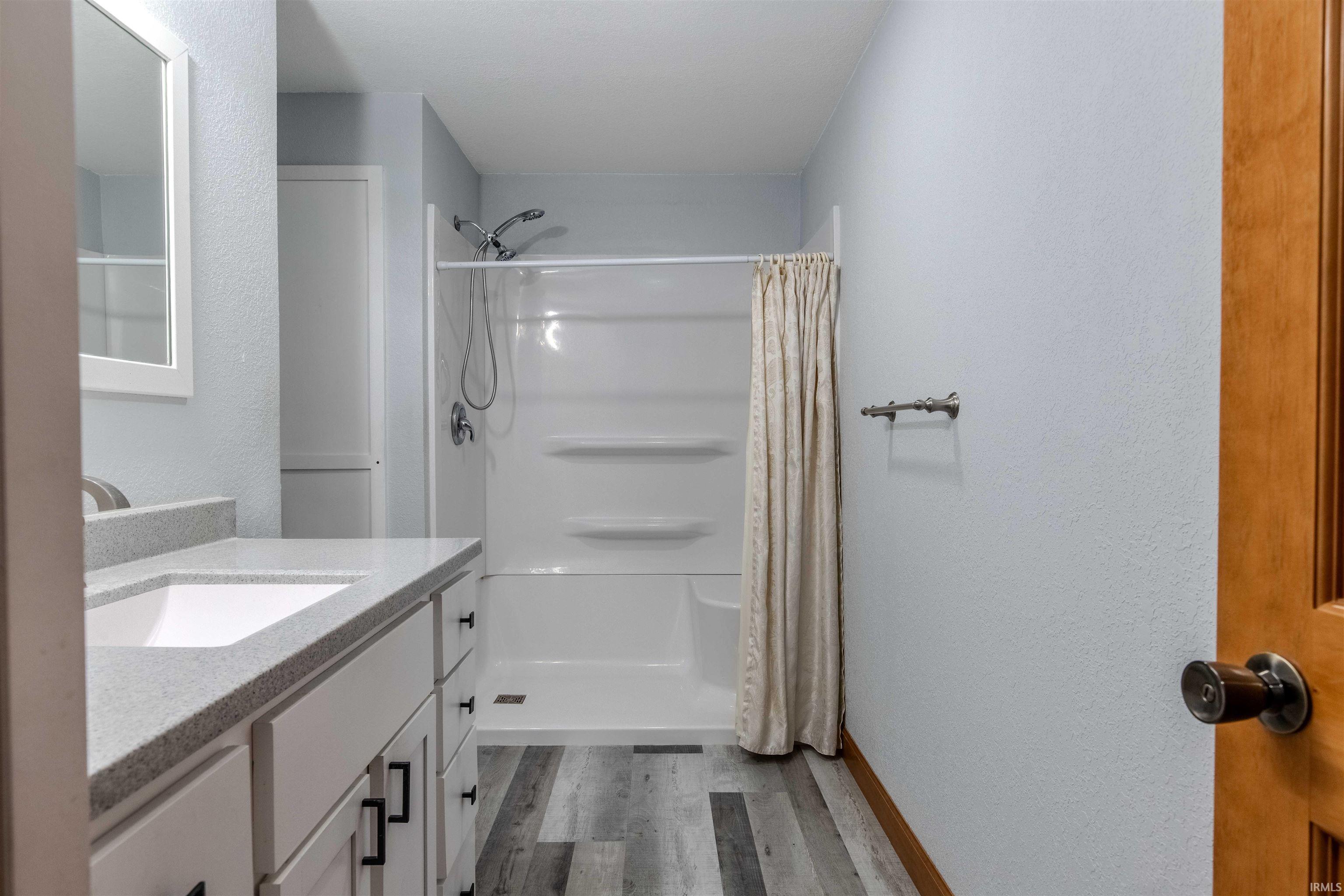 Bathroom with a shower with shower curtain, a textured wall, vanity, and dark wood finished floors