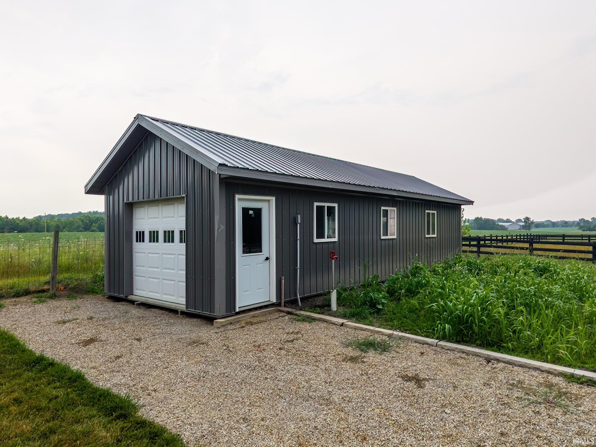 Detached gray structure featuring a white panel garage door, a white entry door, and multiple white-framed windows