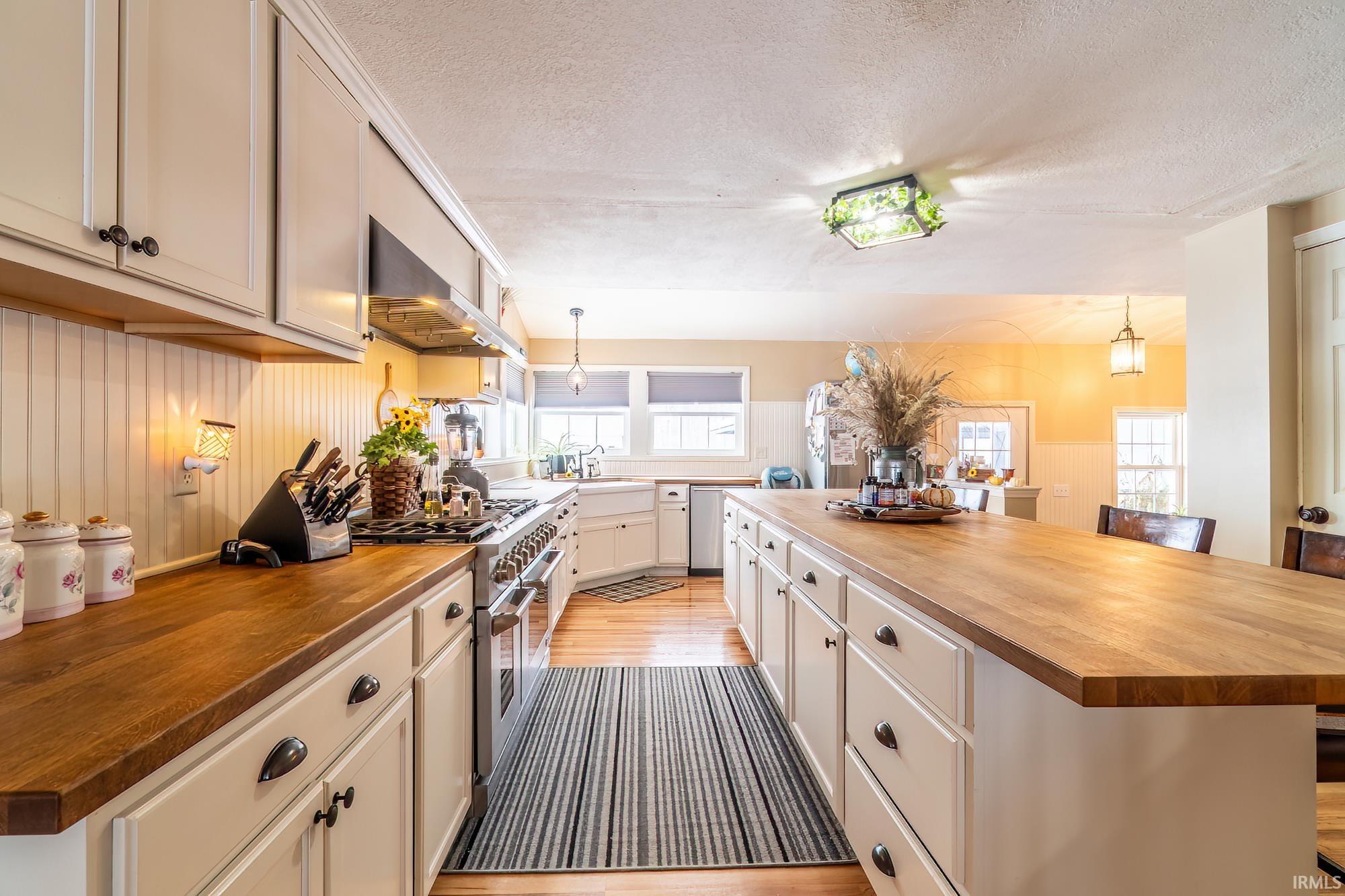 Kitchen featuring butcher block countertops, pendant lighting, range with two ovens, exhaust hood, and a textured ceiling