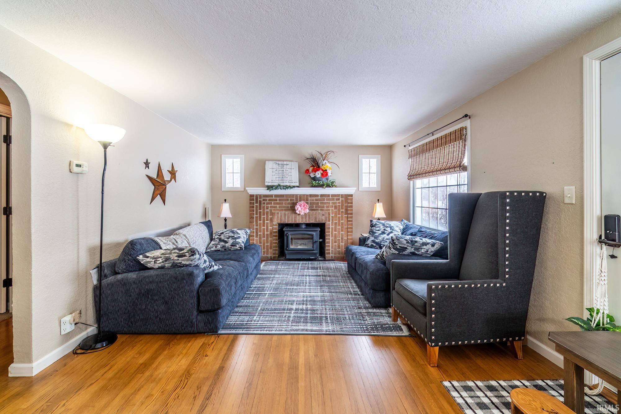 Living room featuring healthy amount of natural light, wood finished floors, arched walkways, a wood stove, and a textured ceiling