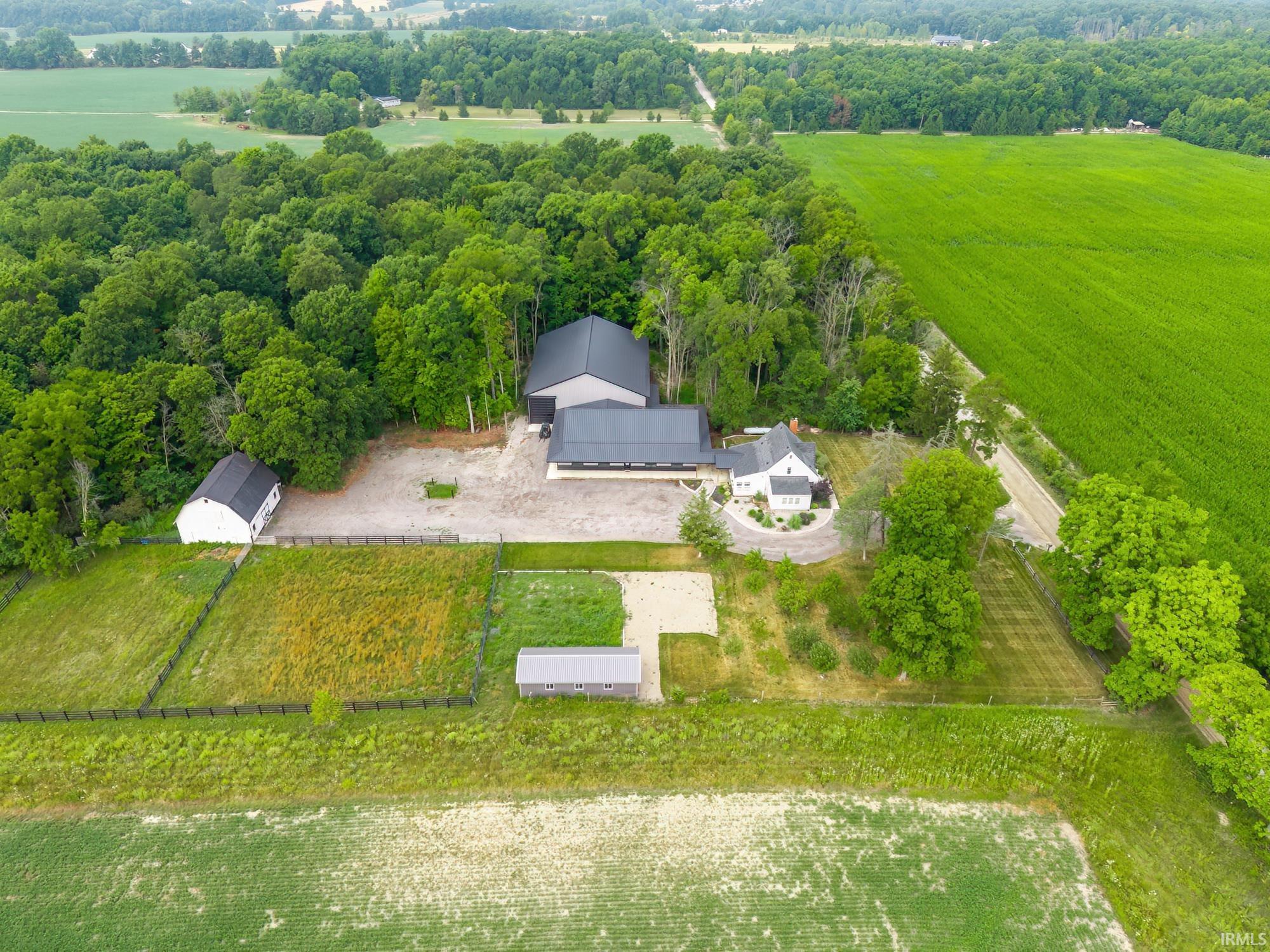 Expansive property featuring a white residence, multiple outbuildings, and a large treed area