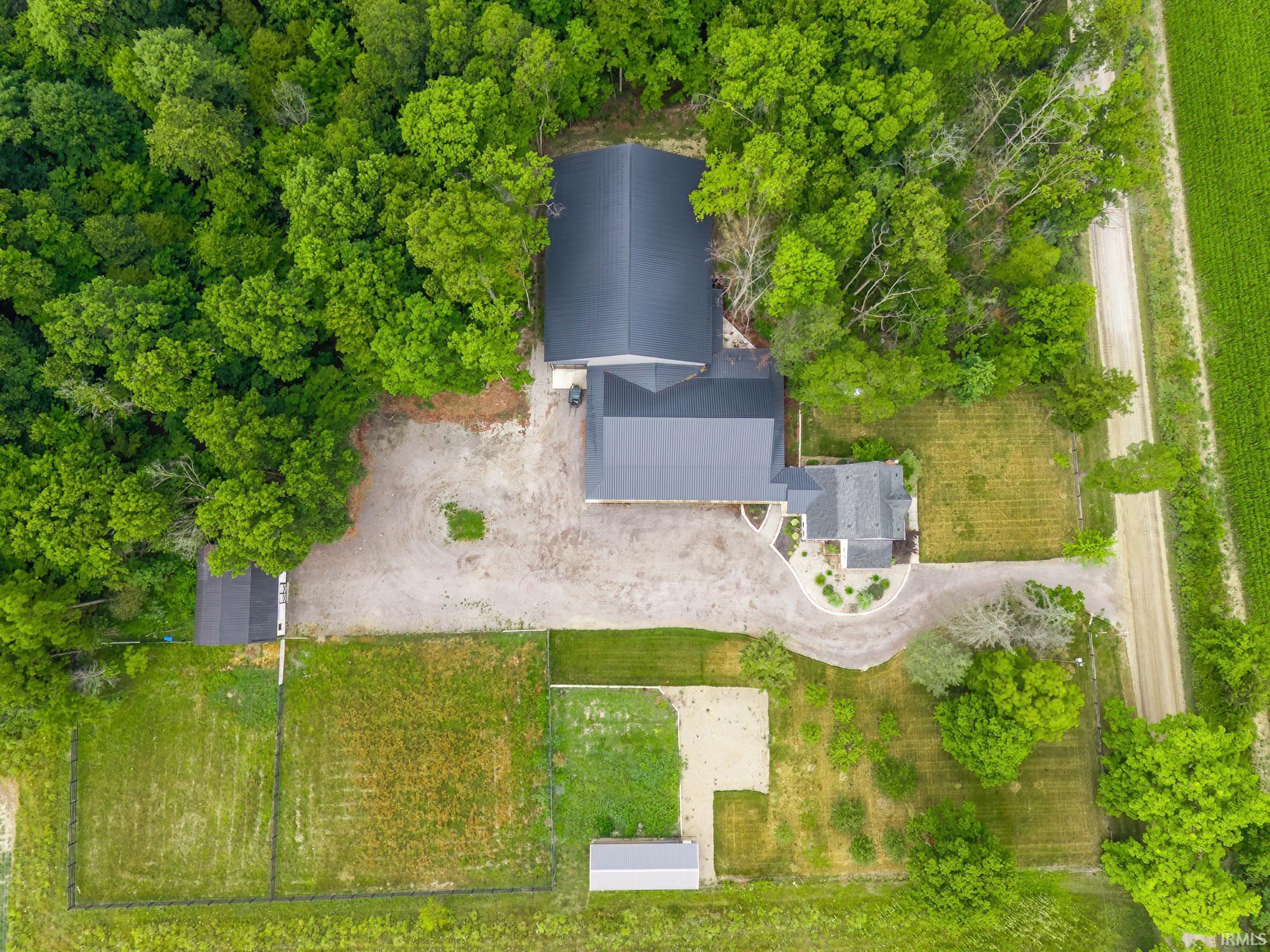 Aerial view showcasing a main residence with a dark gray roof, a detached structure with a dark gray roof, and a smaller outbuilding with a dark gray roof