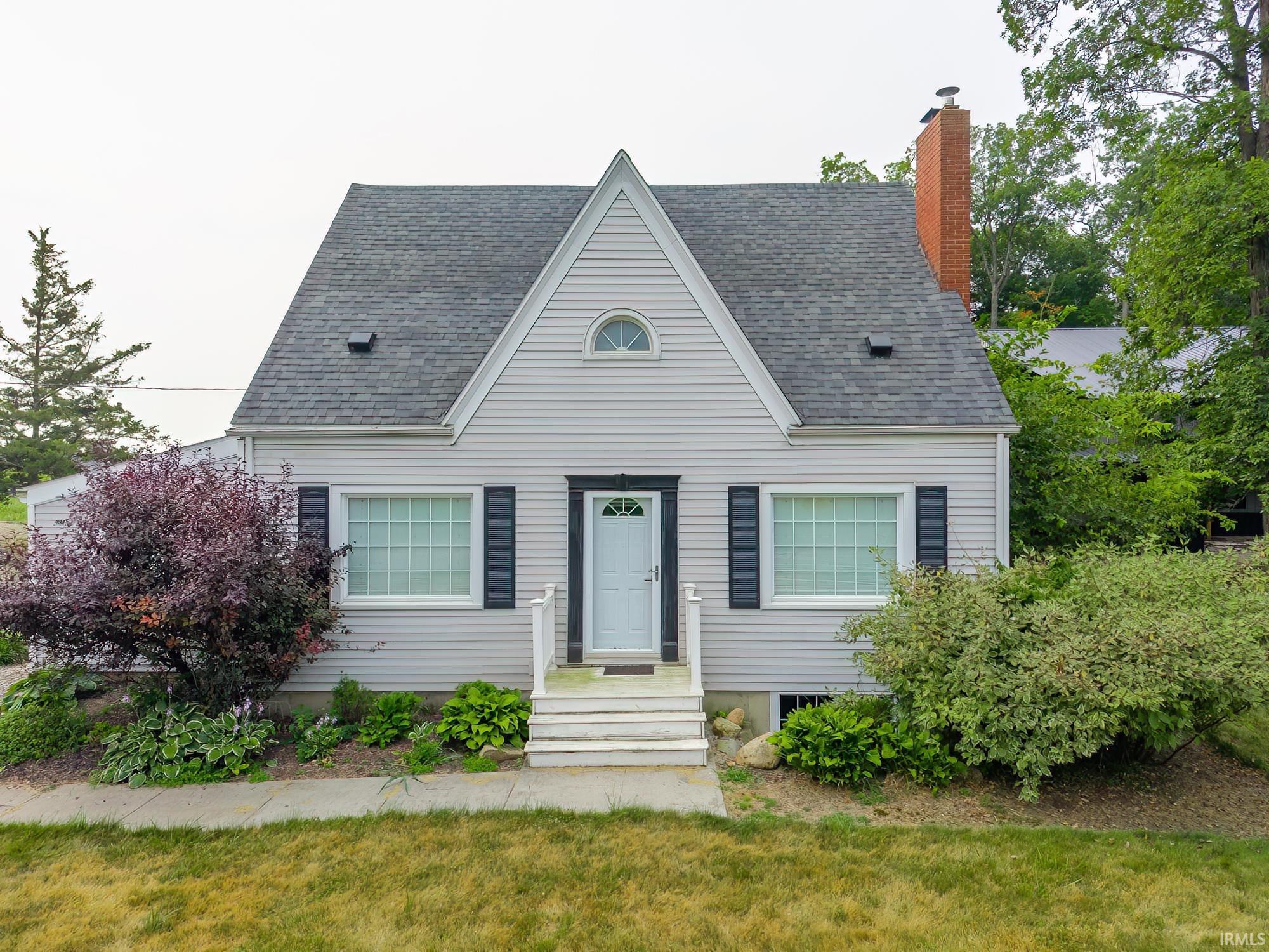 Cape Cod style residence featuring light gray siding, a prominent front gable with an arched window, and dark contrasting shutters