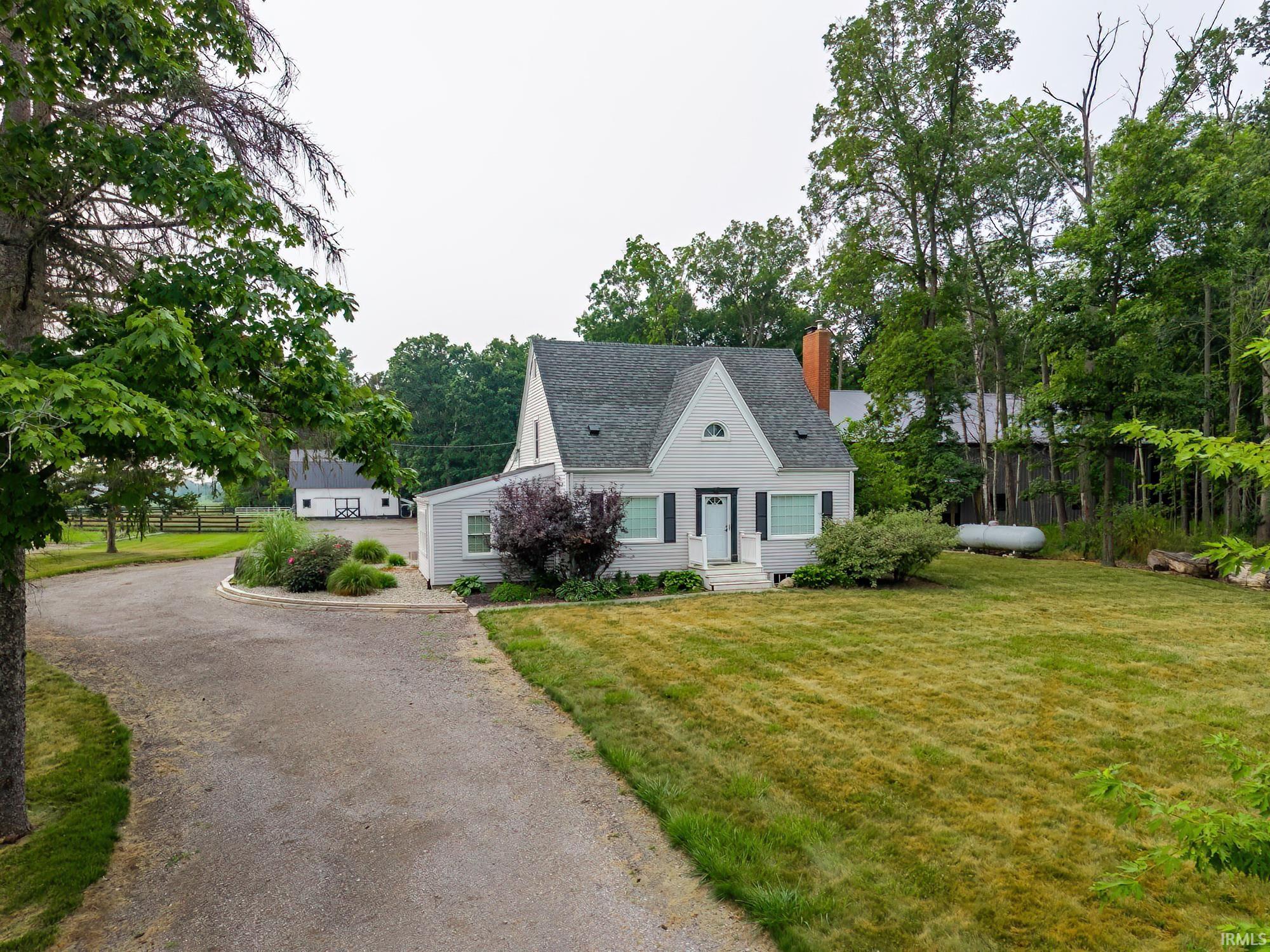 Cape Cod style home featuring a light gray exterior with dark shutters, an asphalt shingle roof, and a prominent red brick chimney