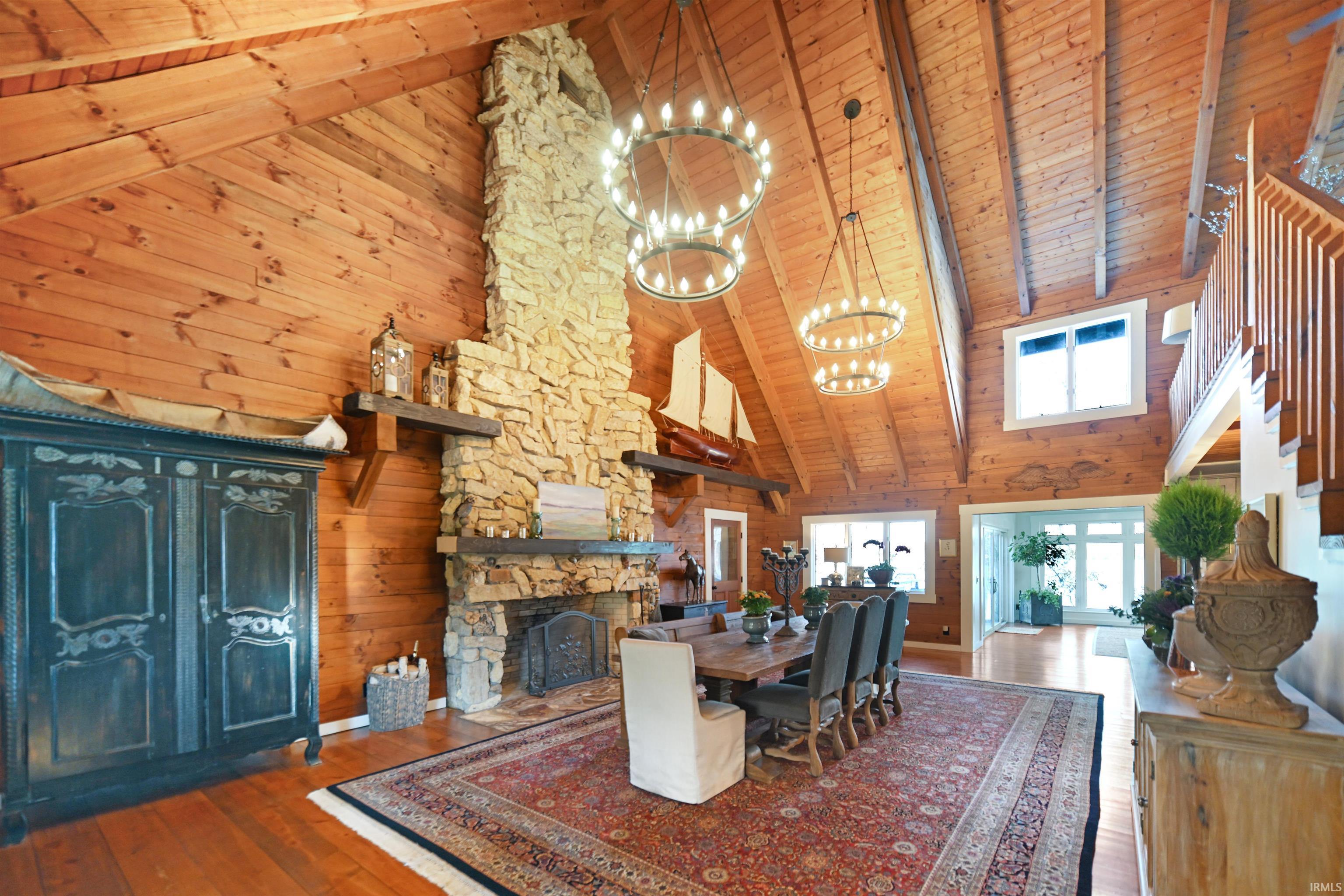 Dining space featuring high vaulted ceiling, wood walls, a wooden ceiling with exposed beams, a stone fireplace, and wood-type flooring