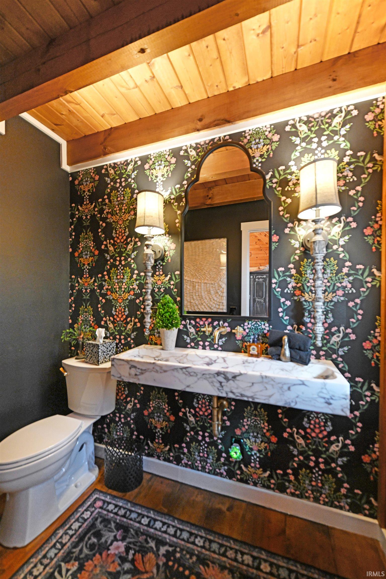 Half bathroom with vanity, a wood ceiling with exposed beams, and wallpapered walls