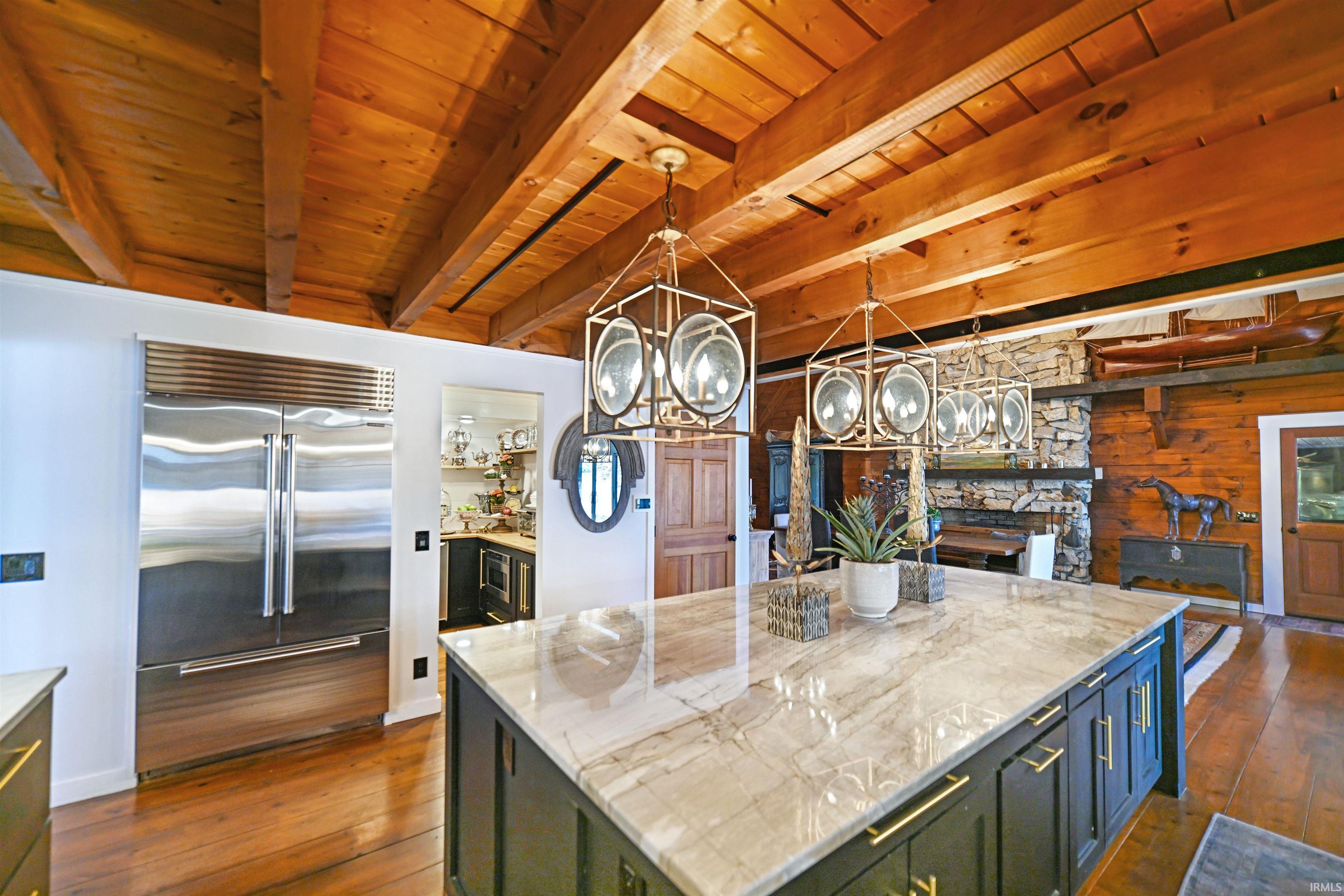 Kitchen featuring pendant lighting, stainless steel built in fridge, dark wood finished floors, a center island, and a wooden ceiling with exposed beams