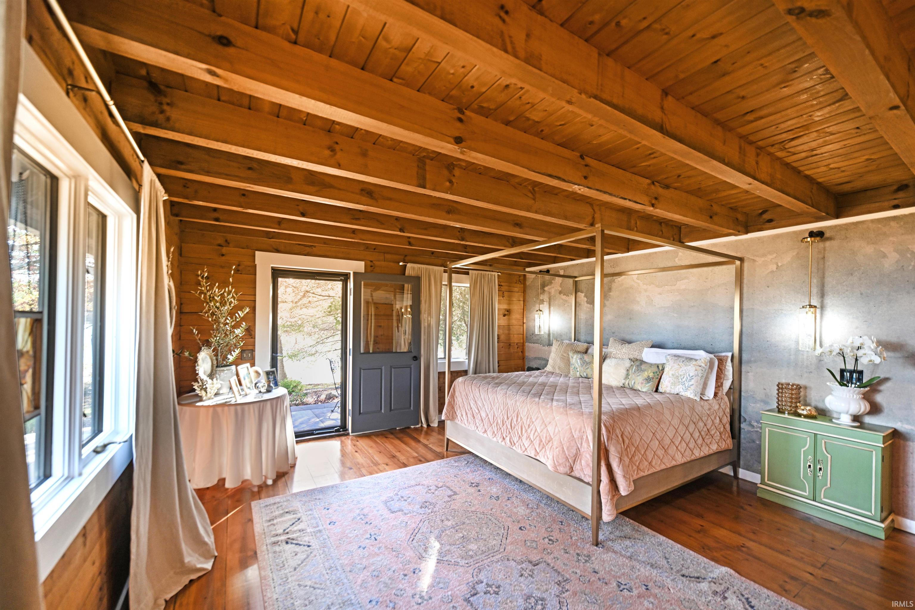 Bedroom with wood-type flooring, access to outside, a wooden ceiling with exposed beams, and wooden walls