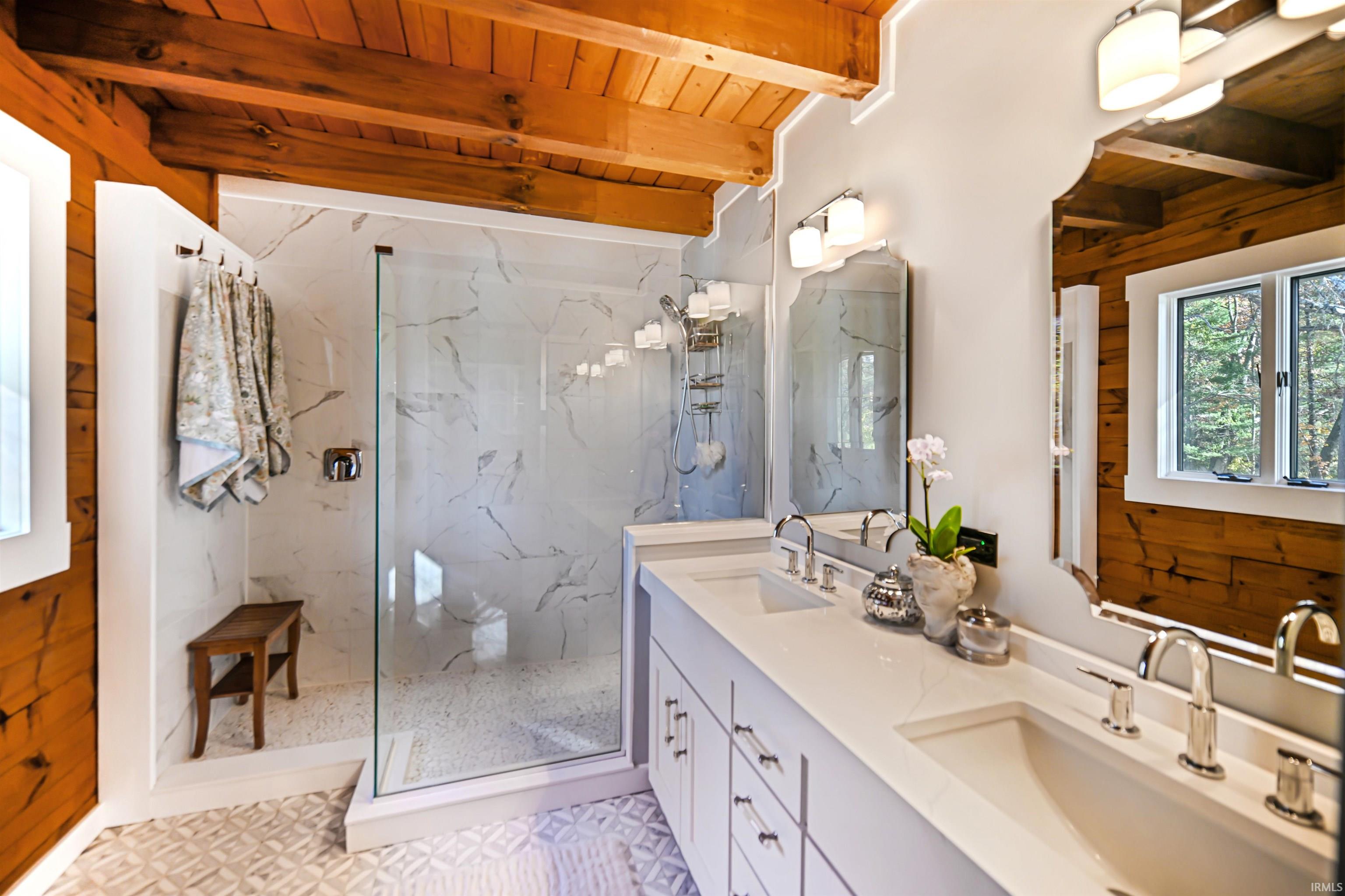 Full bathroom with plenty of natural light, a wooden ceiling with exposed beams, double vanity, and a marble finish shower