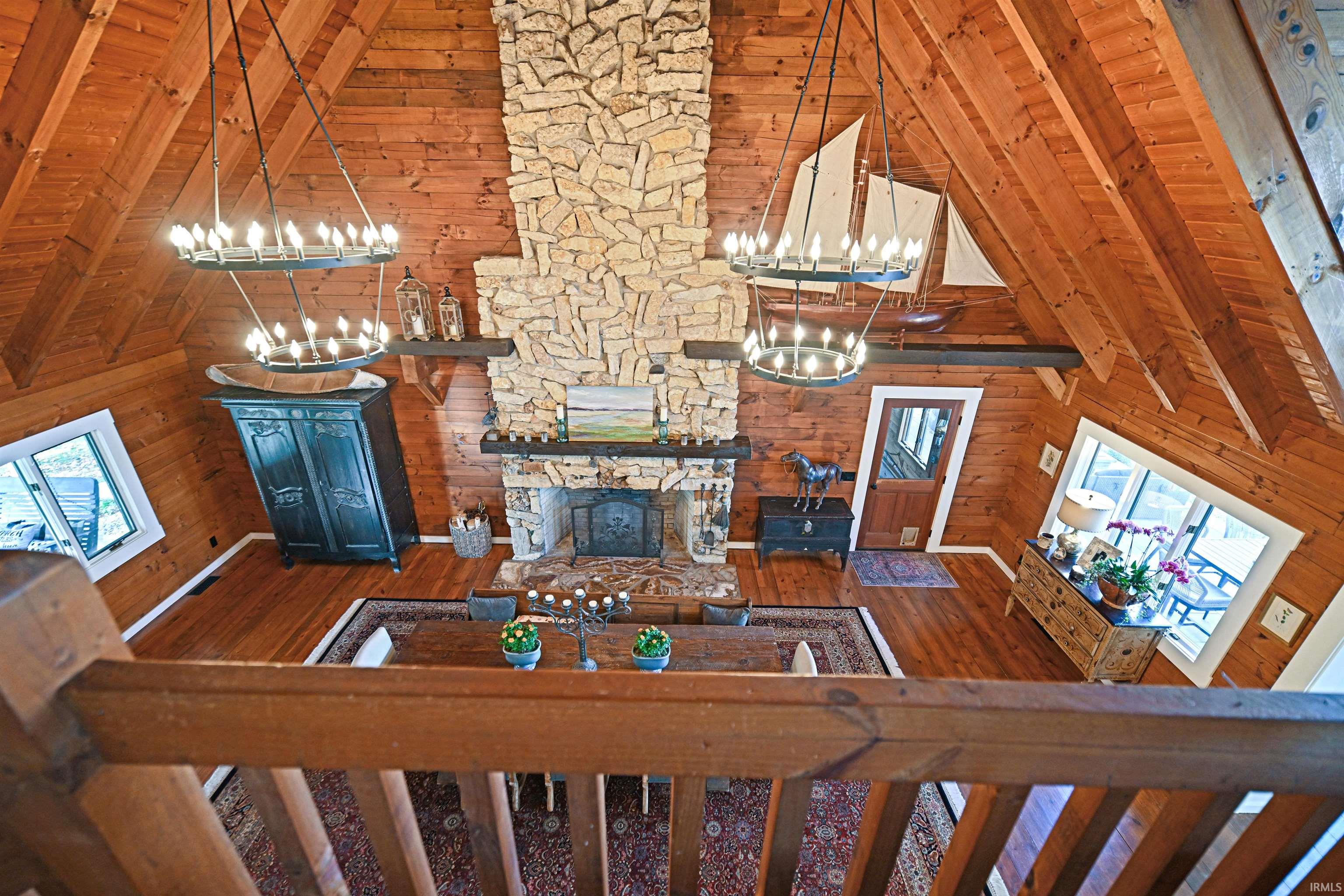 Living room with wood walls, high vaulted ceiling, a stone fireplace, a wooden ceiling with exposed beams, and a chandelier