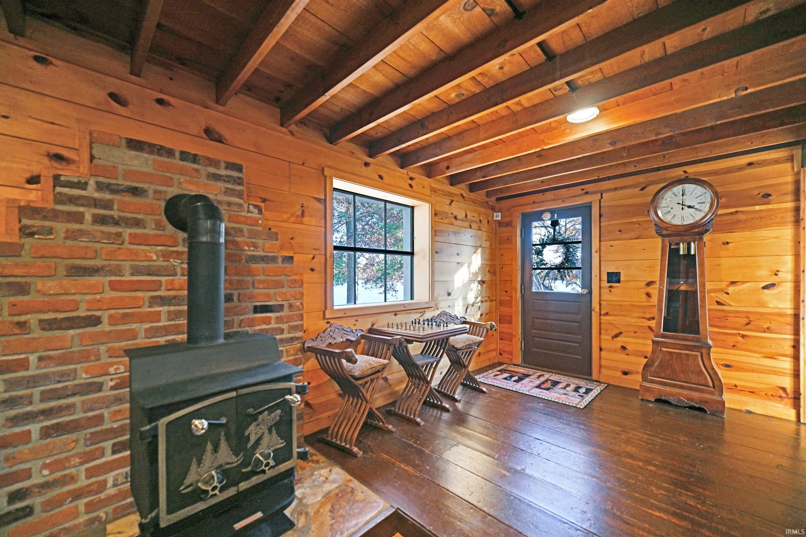 Living room featuring a wood stove, wooden walls, a wooden ceiling with exposed beams, and hardwood / wood-style flooring