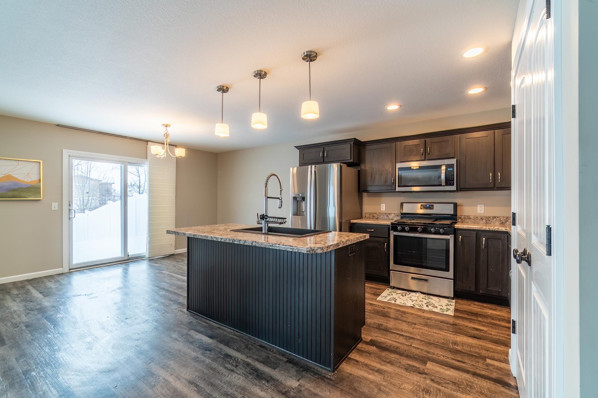 Kitchen featuring appliances with stainless steel finishes, a kitchen island with sink, dark brown cabinets, pendant lighting, and dark wood-style floors
