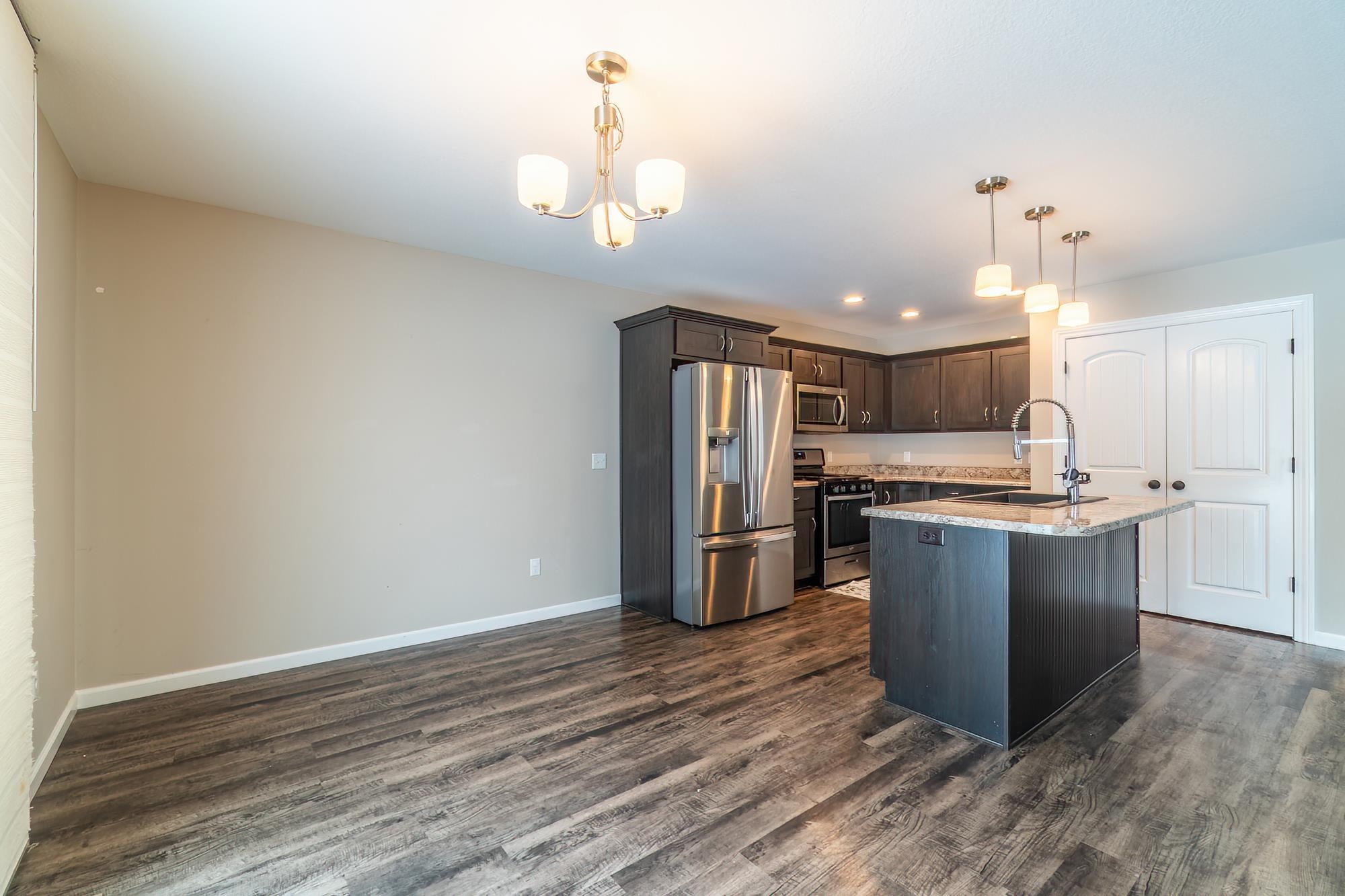 Kitchen with dark brown cabinets, appliances with stainless steel finishes, decorative light fixtures, a kitchen island with sink, and a chandelier