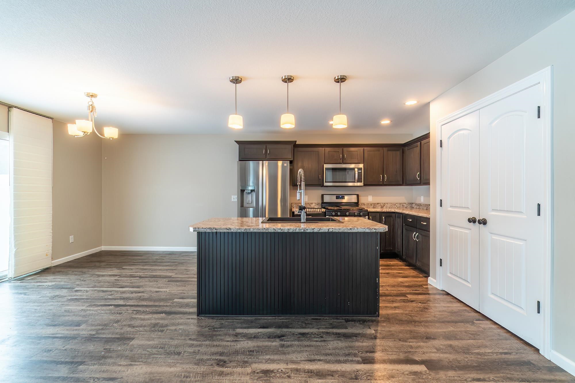 Kitchen with dark brown cabinetry, stainless steel appliances, pendant lighting, an island with sink, and dark wood-style floors
