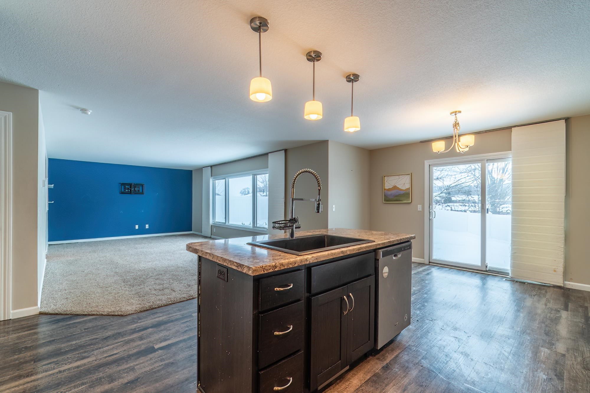 Kitchen featuring dark brown cabinets, an island with sink, decorative light fixtures, stainless steel dishwasher, and a textured ceiling