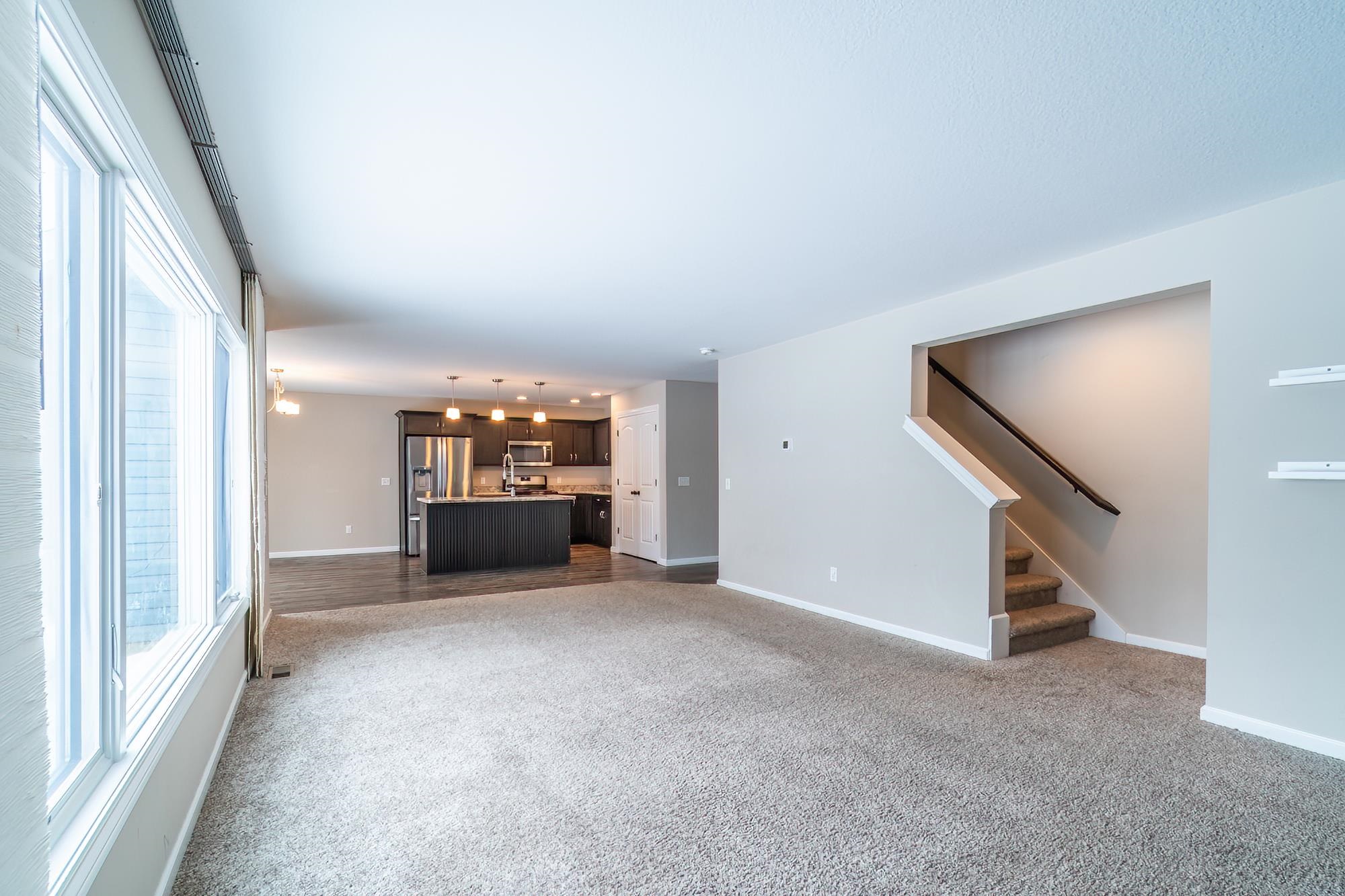 Unfurnished living room with dark colored carpet and stairway