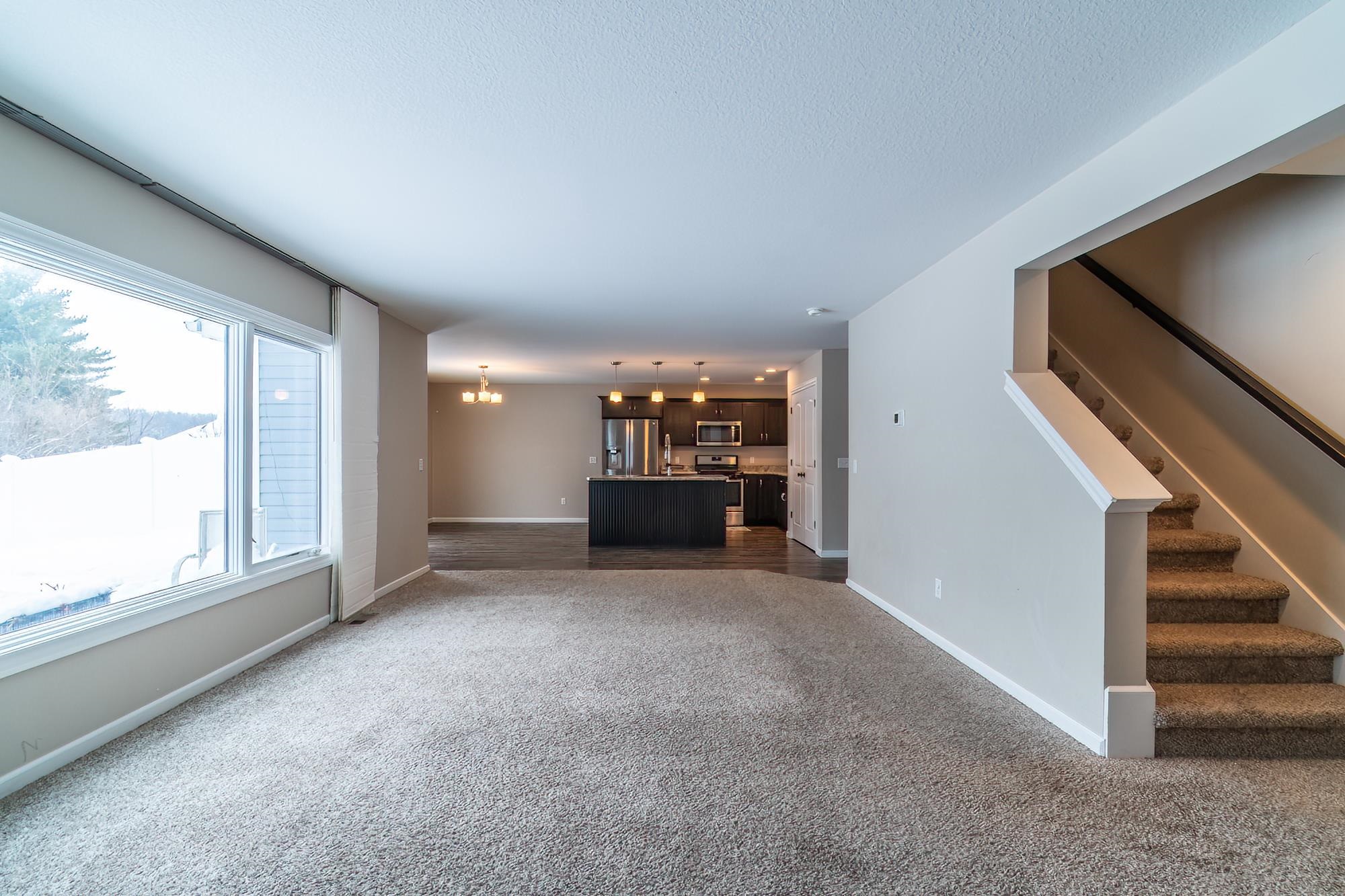 Unfurnished living room with dark carpet, a chandelier, and stairs