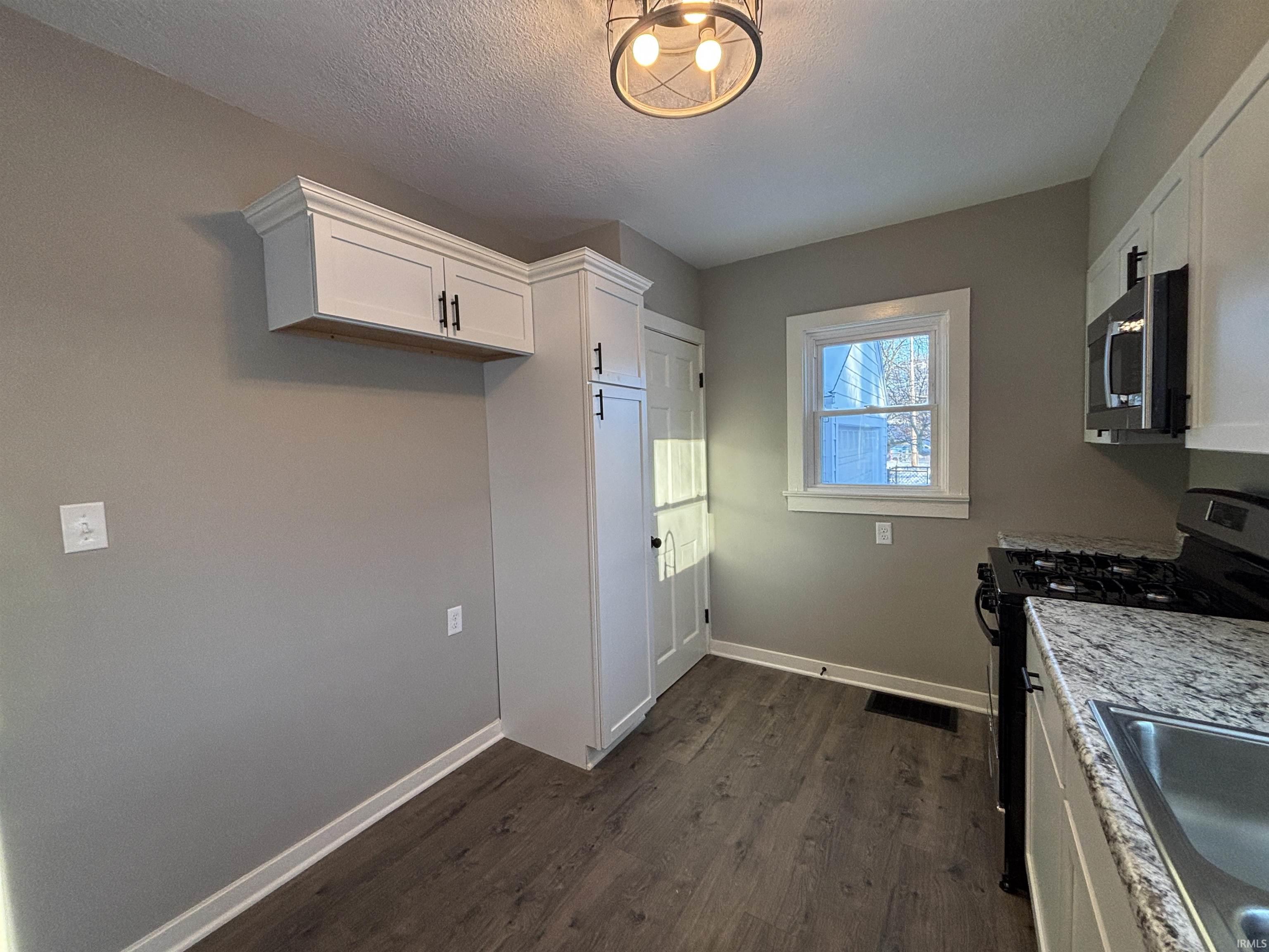 Kitchen featuring gas range, white cabinetry, stainless steel microwave, dark wood-type flooring, and a textured ceiling