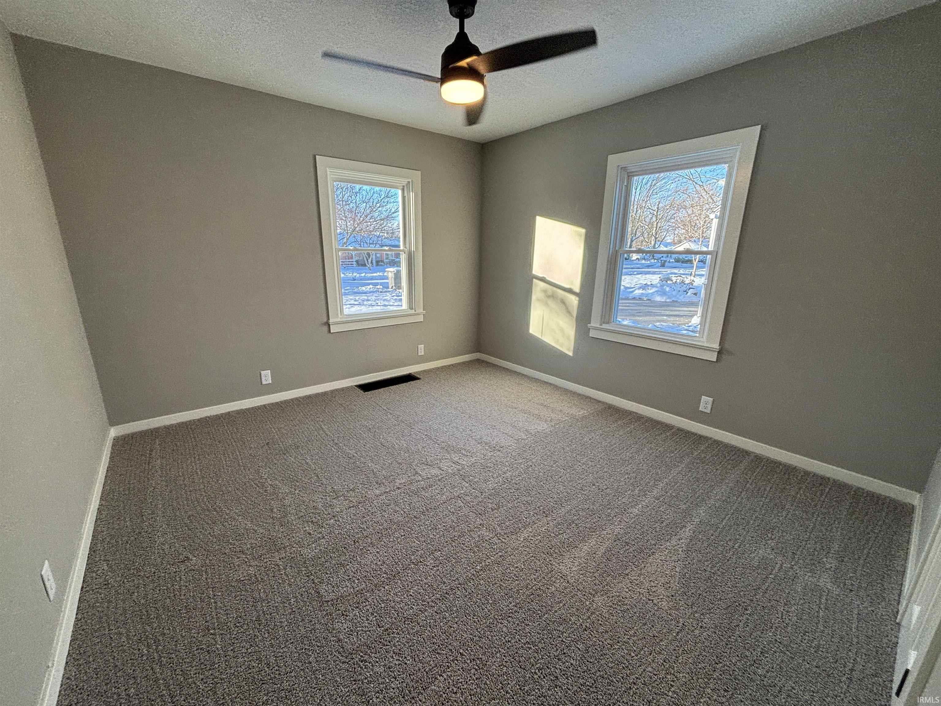 Carpeted spare room featuring healthy amount of natural light, a textured ceiling, and a ceiling fan