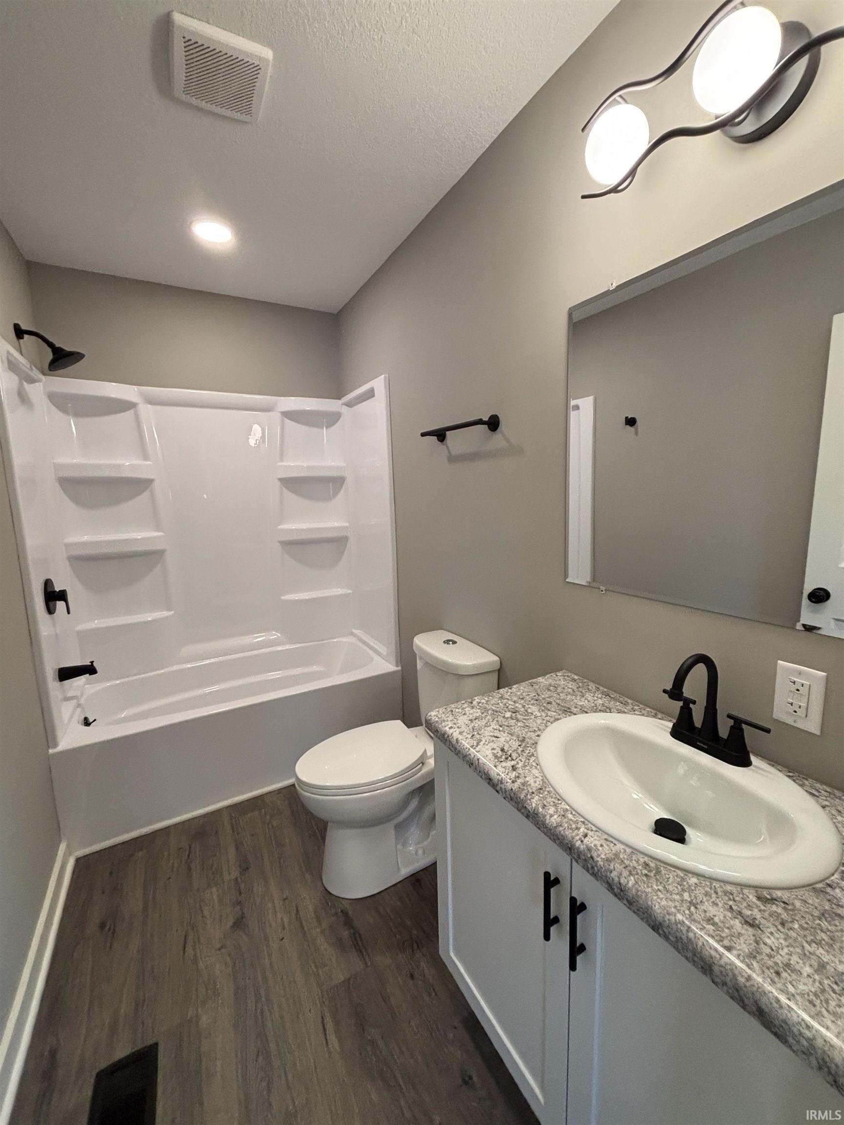 Bathroom with vanity, shower / tub combination, dark wood-style flooring, and a textured ceiling