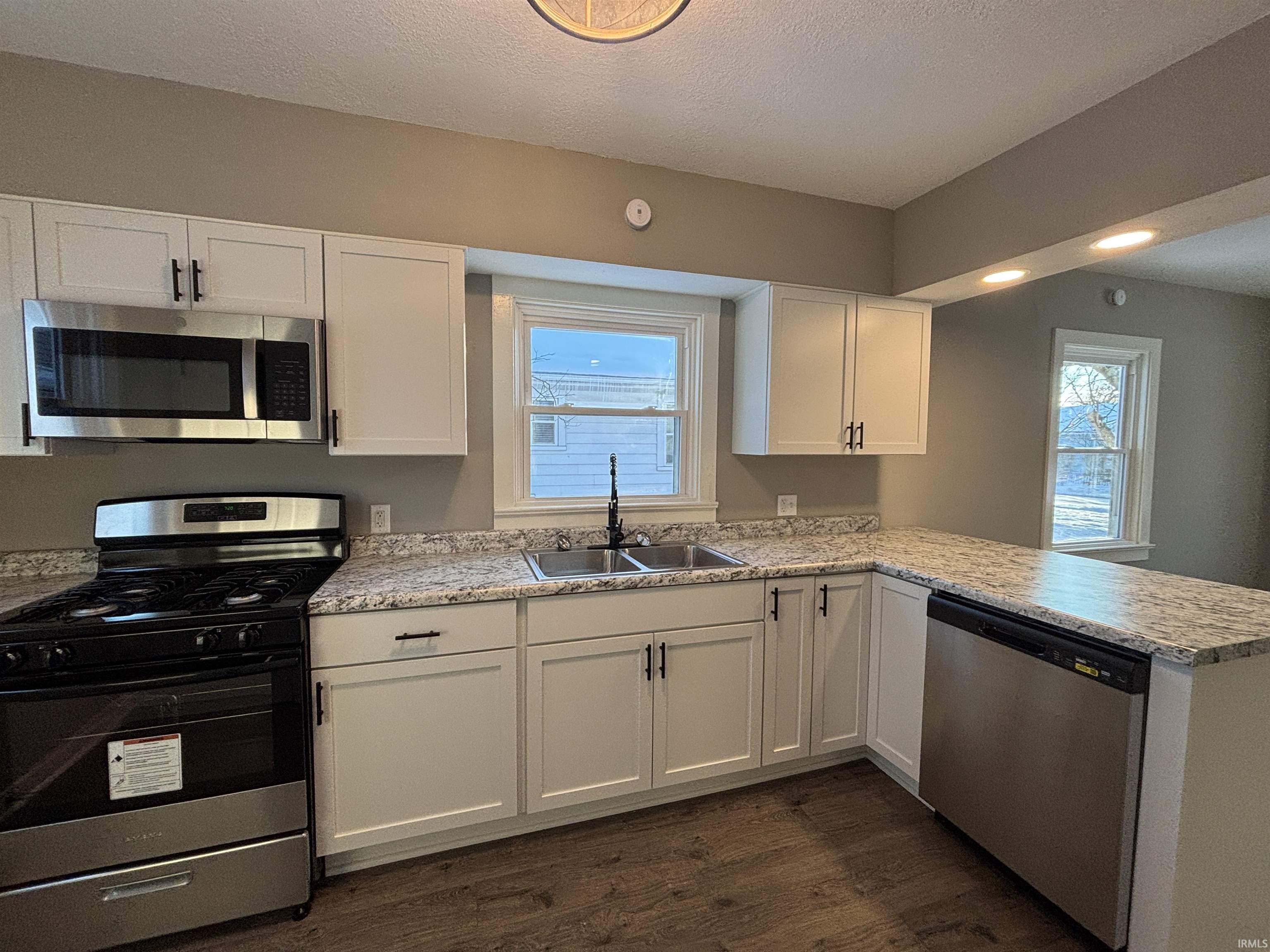 Kitchen featuring stainless steel appliances, white cabinets, a peninsula, dark wood-style floors, and a textured ceiling