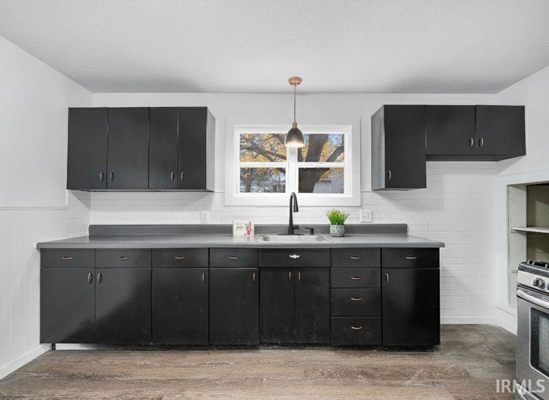 Kitchen with dark cabinetry, decorative light fixtures, light wood finished floors, stainless steel gas range, and wainscoting