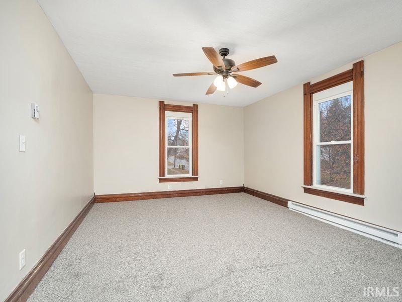 Unfurnished room featuring light colored carpet, baseboard heating, and a ceiling fan