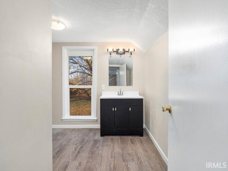 Bathroom with vanity, light wood-style flooring, a textured ceiling, and vaulted ceiling