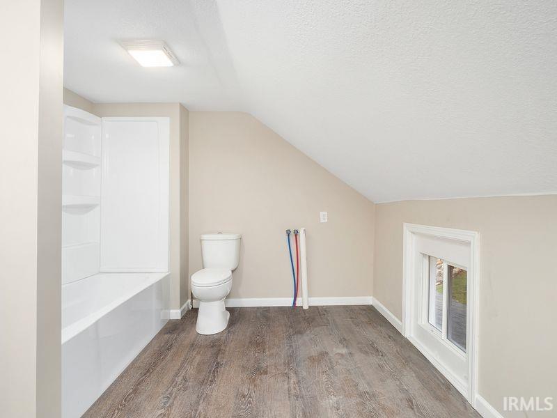 Bathroom with lofted ceiling, wood finished floors, a textured ceiling, and tub / shower combination