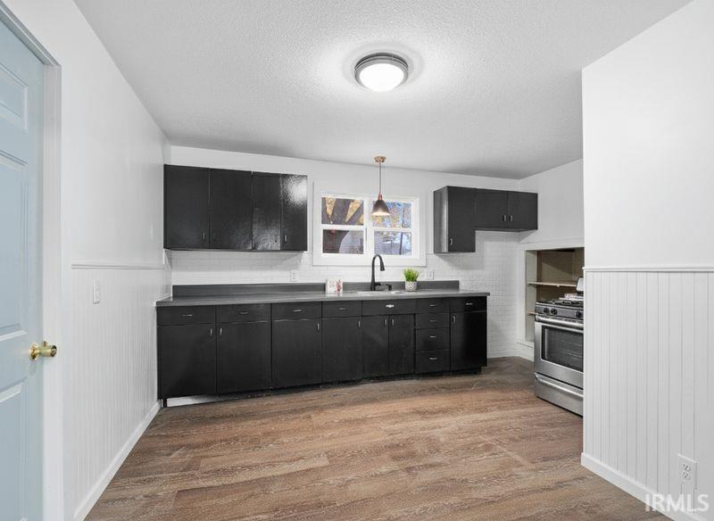 Kitchen featuring wainscoting, dark cabinetry, stainless steel gas stove, a textured ceiling, and decorative light fixtures