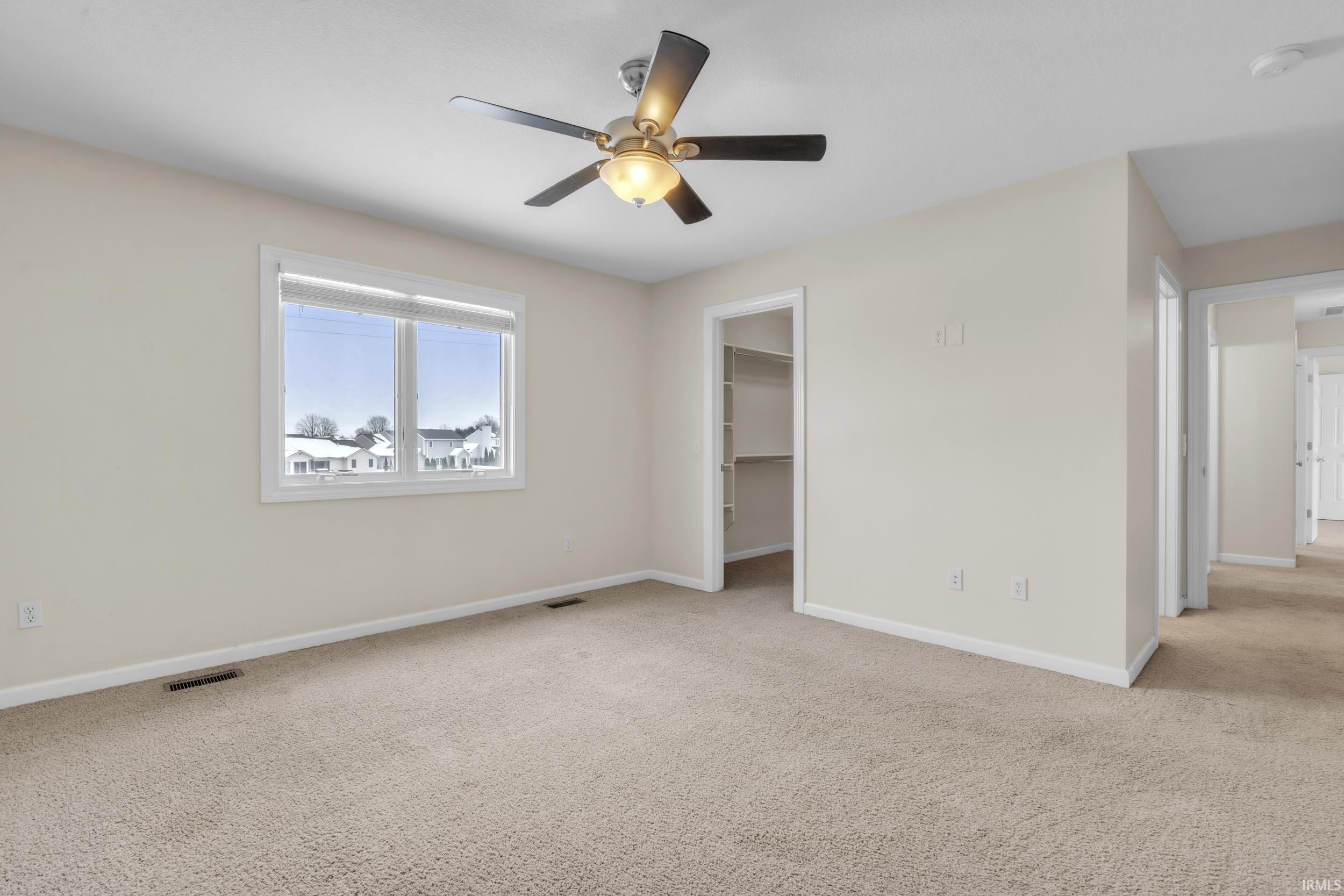 Unfurnished bedroom featuring light colored carpet, a spacious closet, and ceiling fan