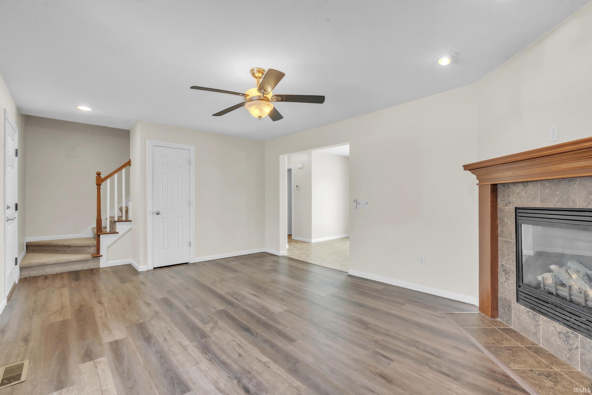 Unfurnished living room featuring a tiled fireplace, recessed lighting, stairs, light wood-style floors, and ceiling fan
