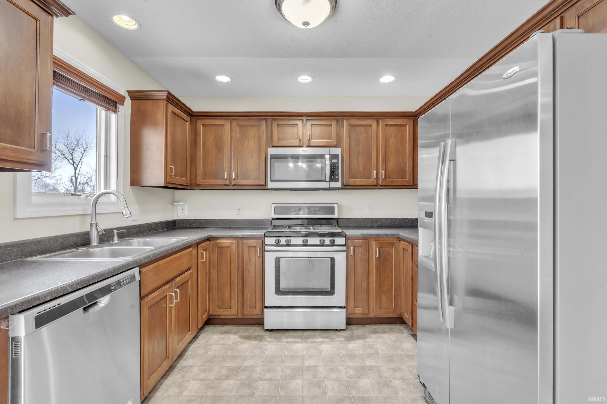 Kitchen featuring stainless steel appliances, brown cabinets, dark countertops, and recessed lighting